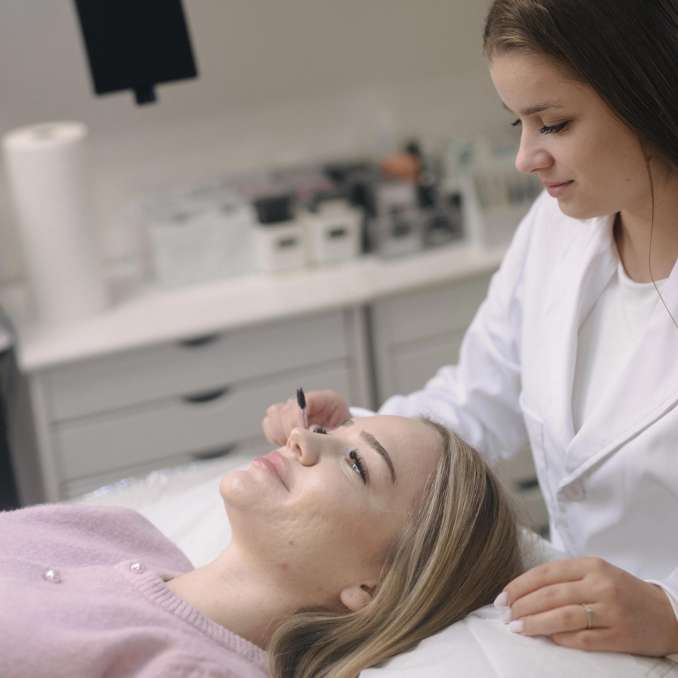A beauty professional applies an eyelash treatment to a client.