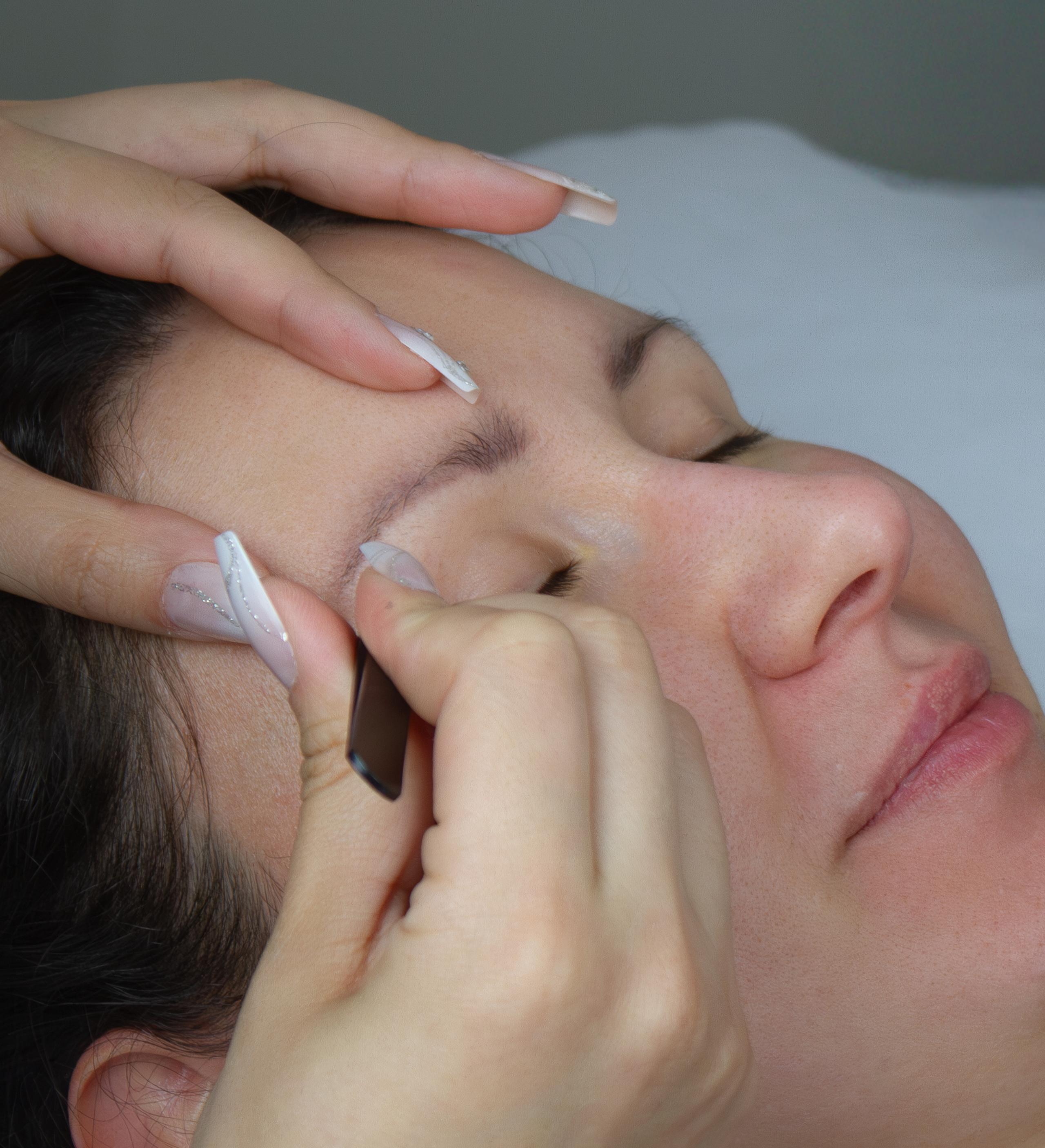 A beauty technician carefully shapes a client's eyebrow.