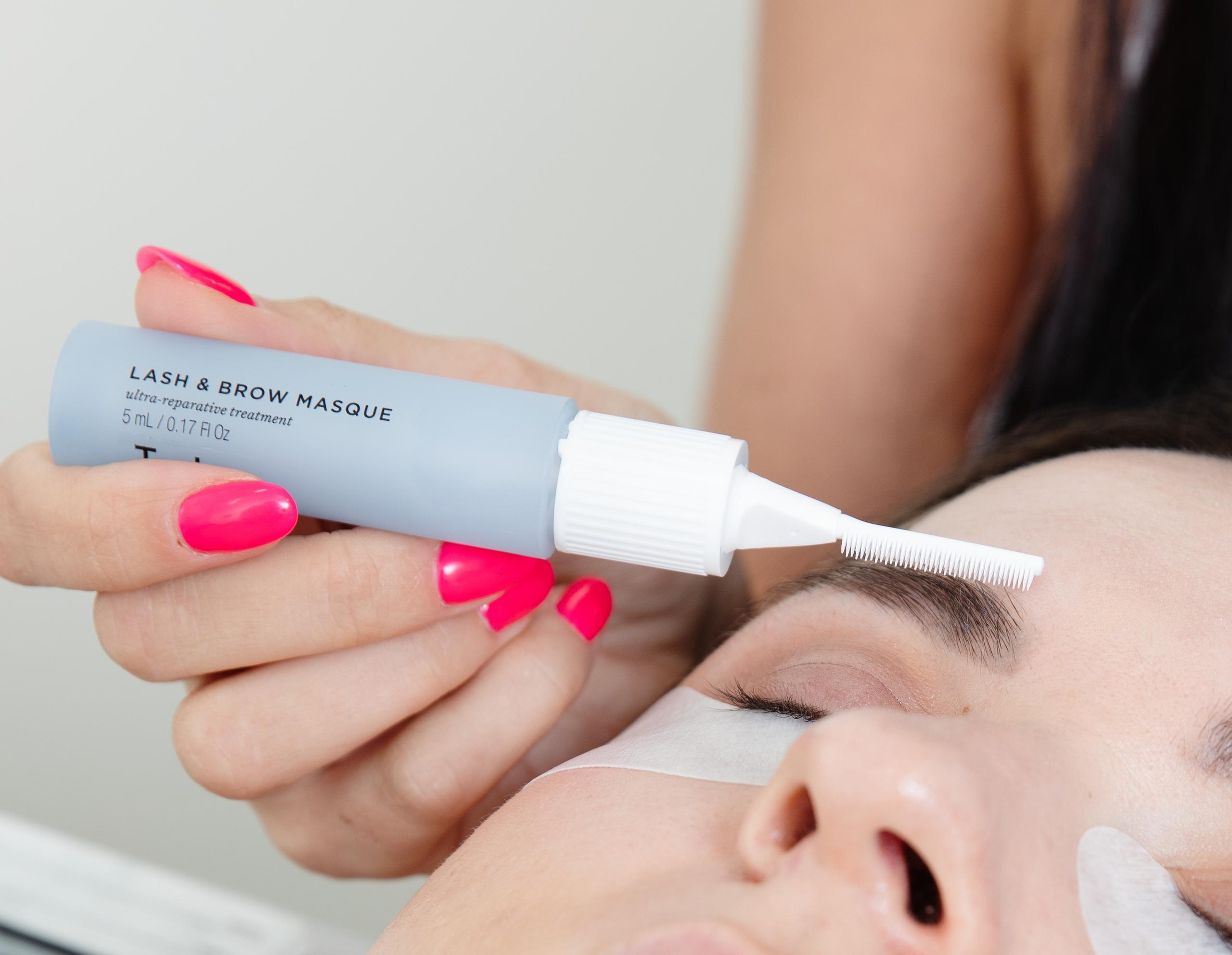 Lash and brow conditioning mask being applied to a client's eyebrow with a brush applicator.