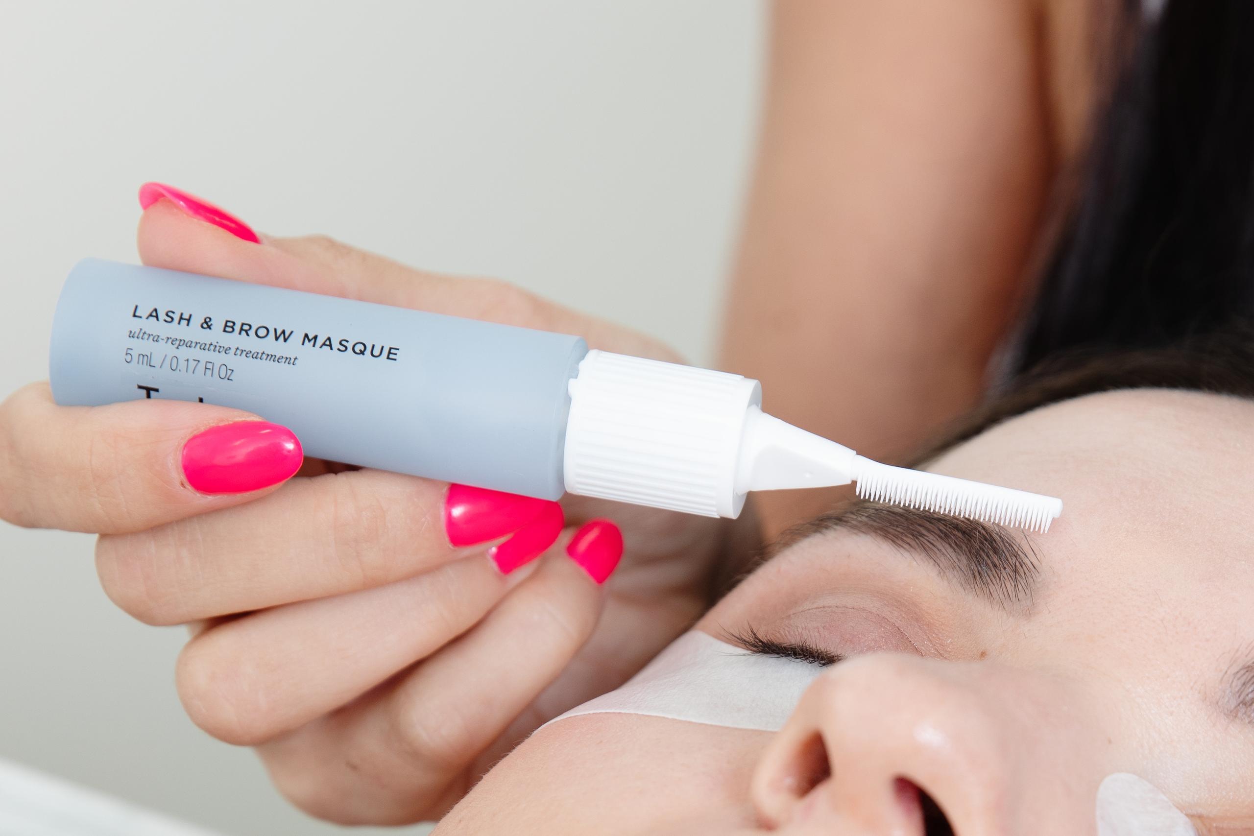 Lash and brow conditioning mask being applied to a client's eyebrow with a brush applicator.
