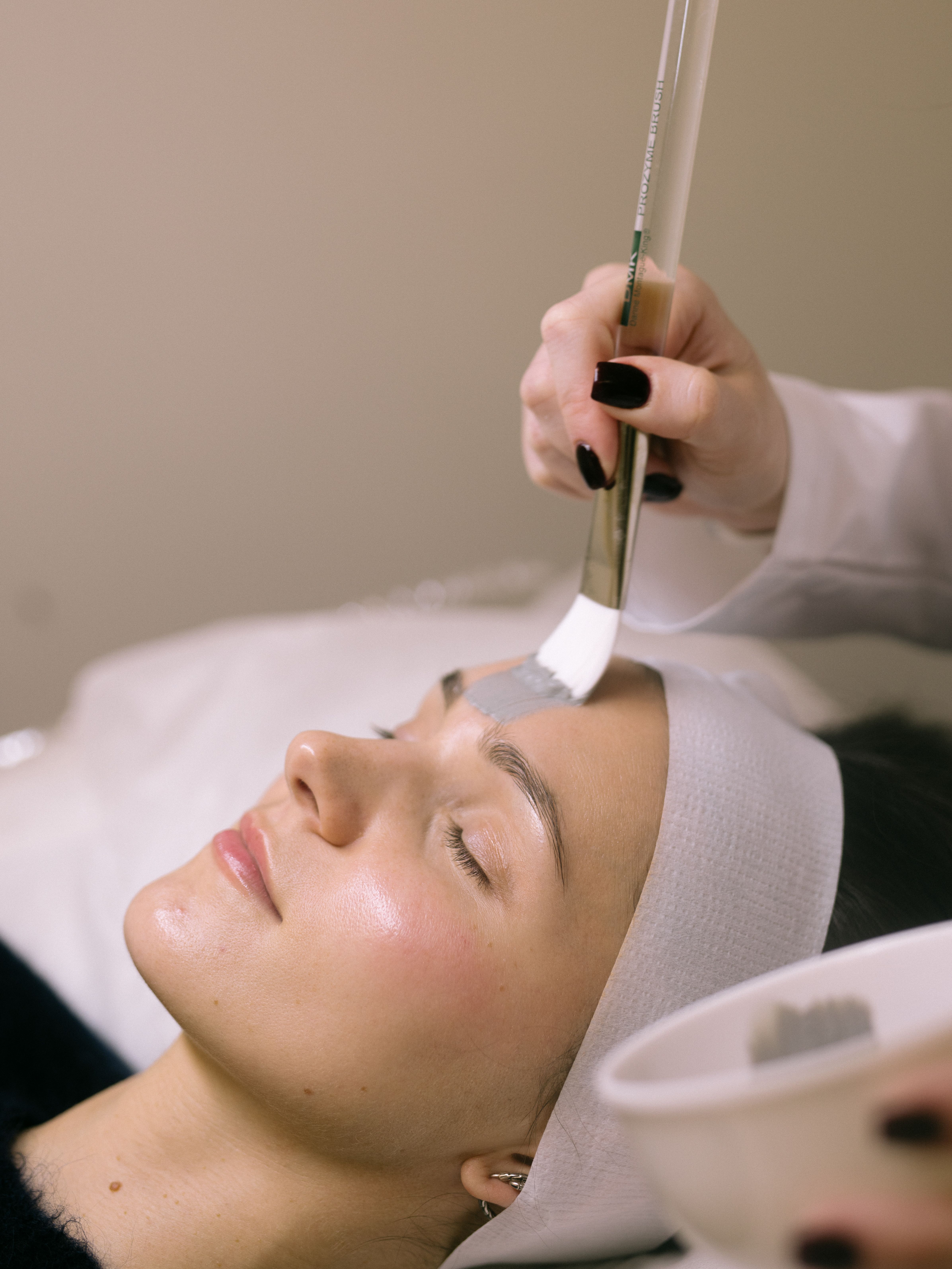 Close-up of a mask being brushed onto a client’s forehead during a facial.