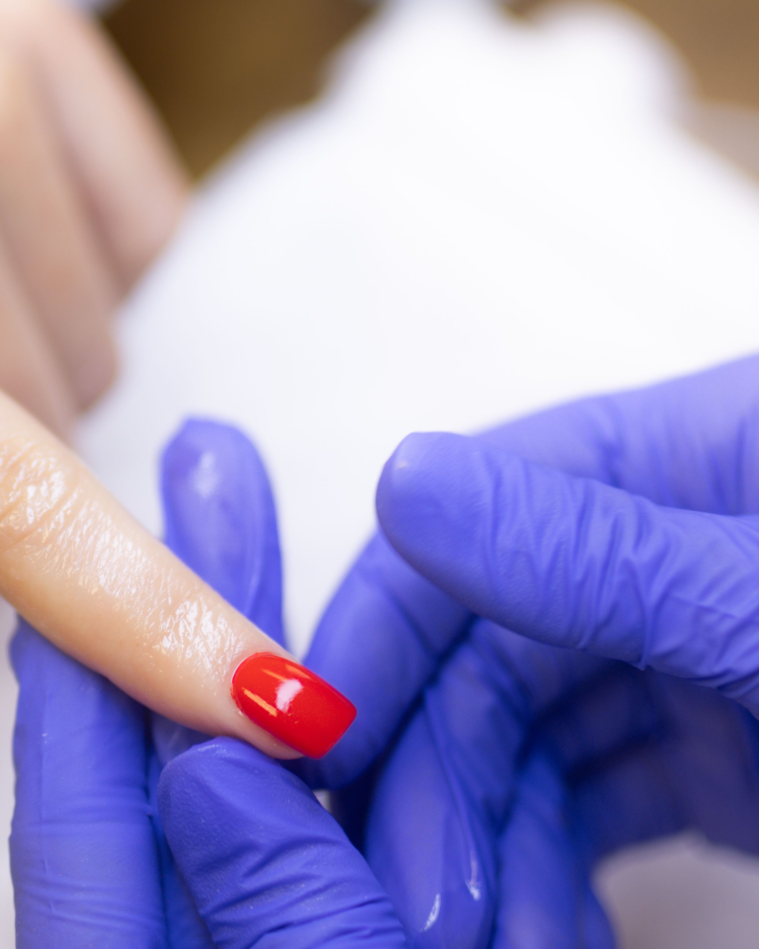 Close-up of a hand in a blue glove holding a finger with a shiny red polished nail.