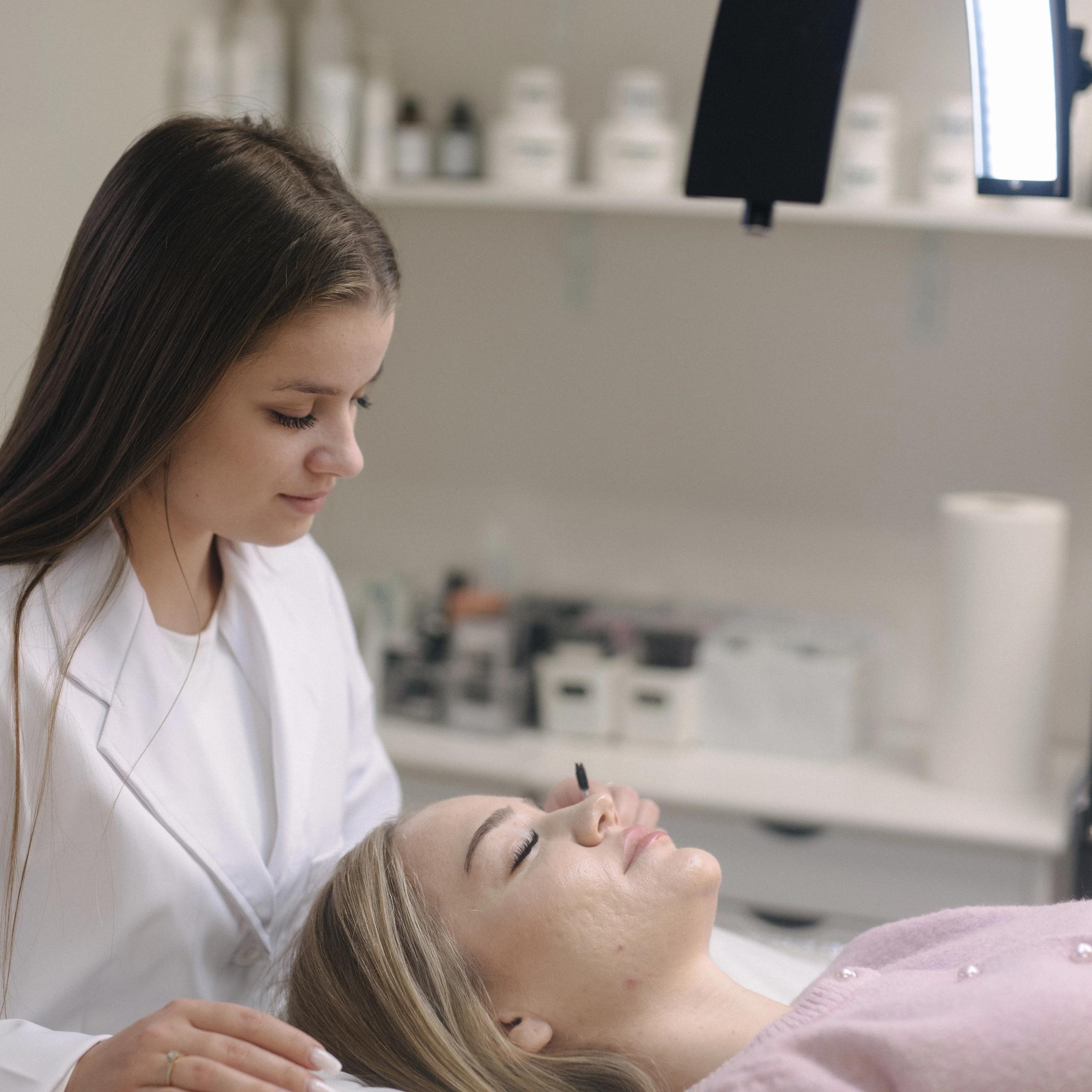 A beauty technician applies eyelash extensions to a client in a salon.