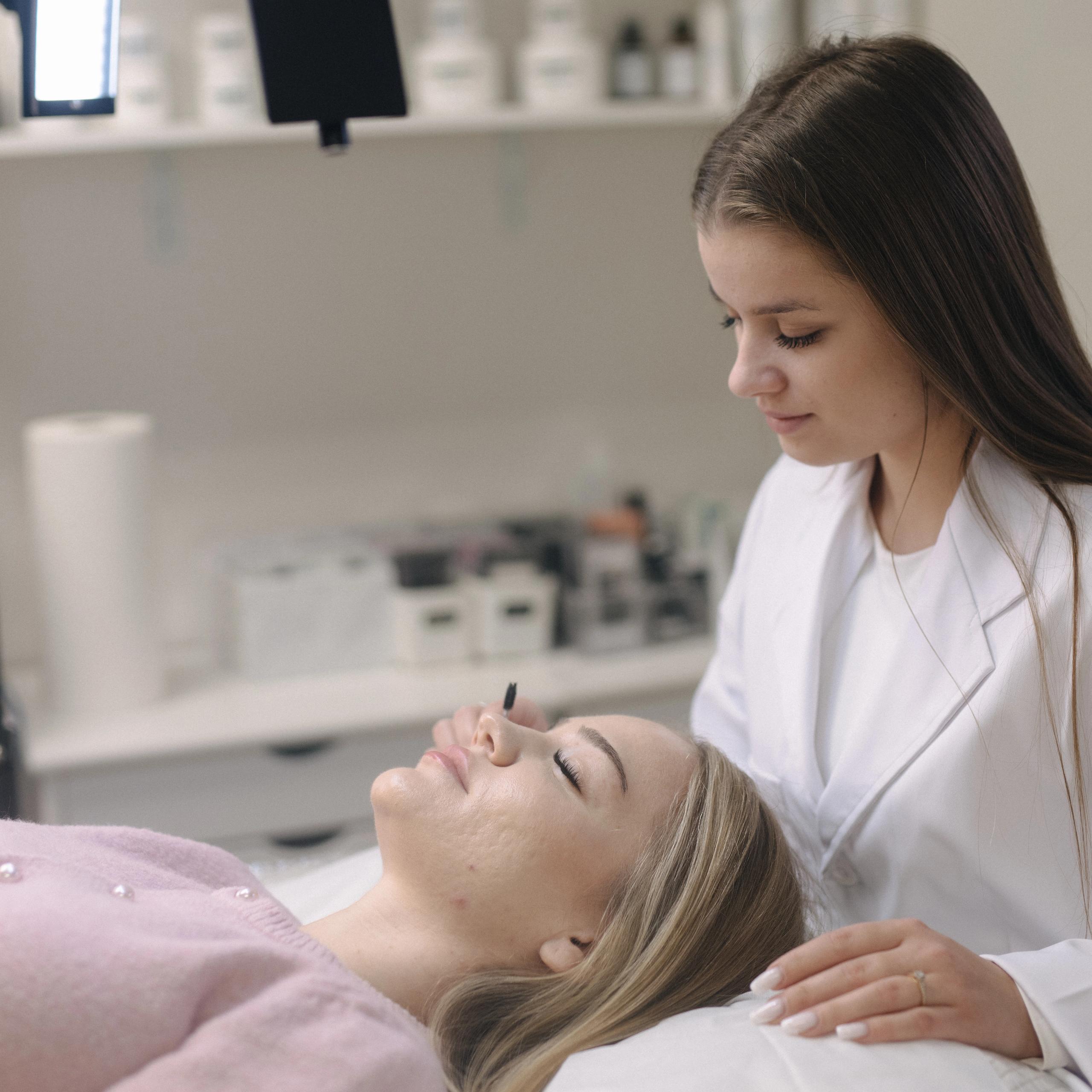 A lash artist applies an eyelash treatment to a client lying down.