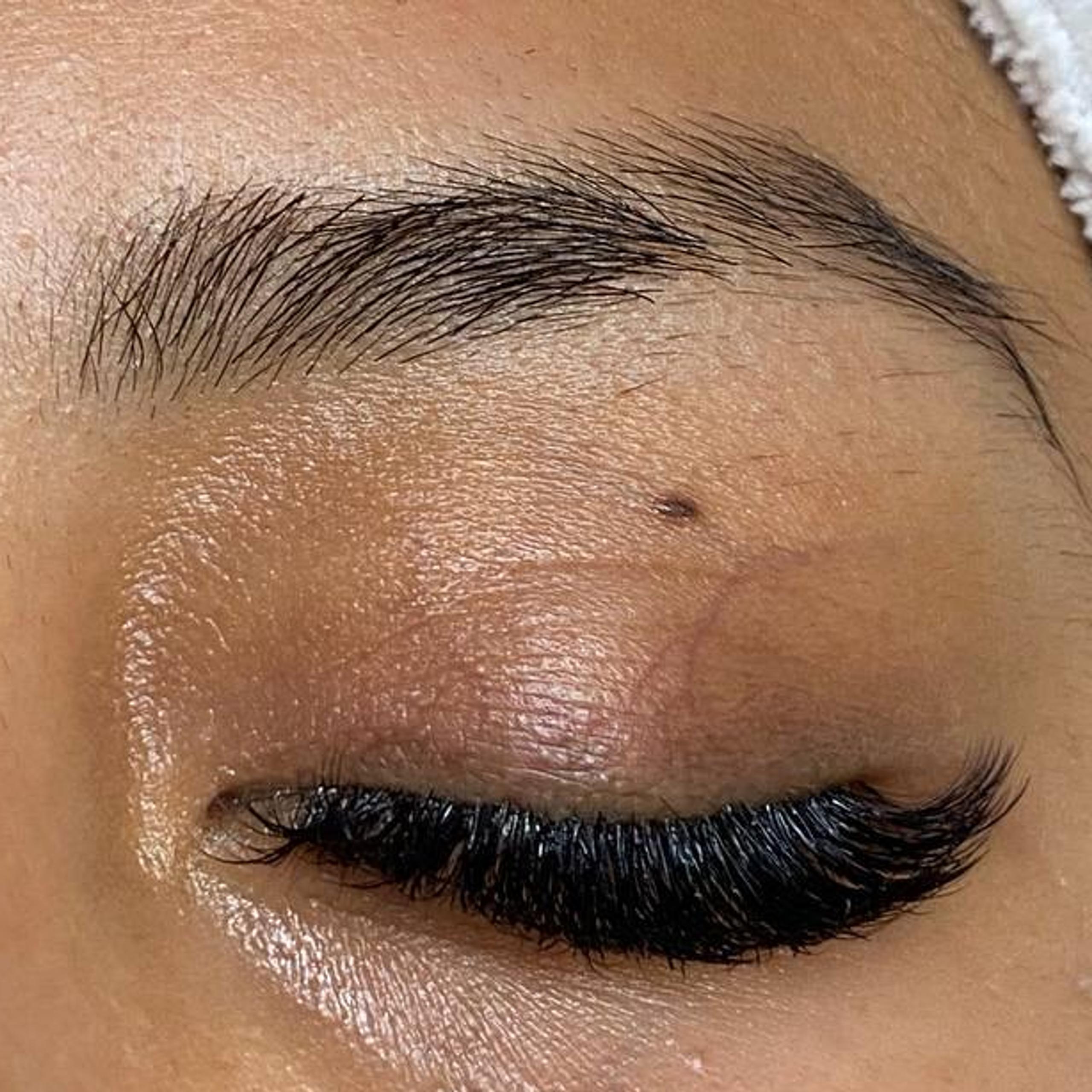 A close-up of a person's closed eye with voluminous eyelashes and natural eyebrows