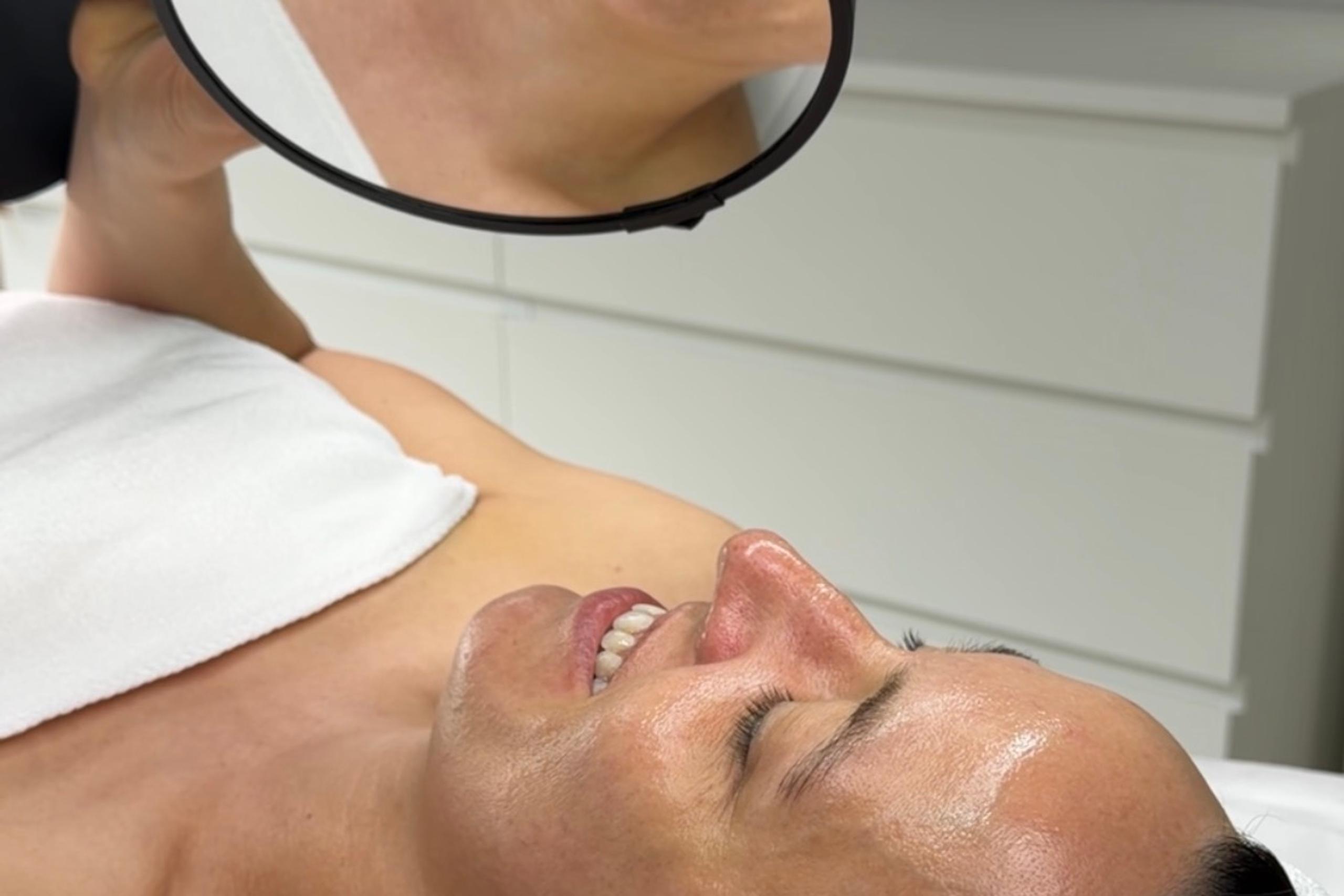 A gloved hand brushes a woman's eyebrow with a spoolie brush.