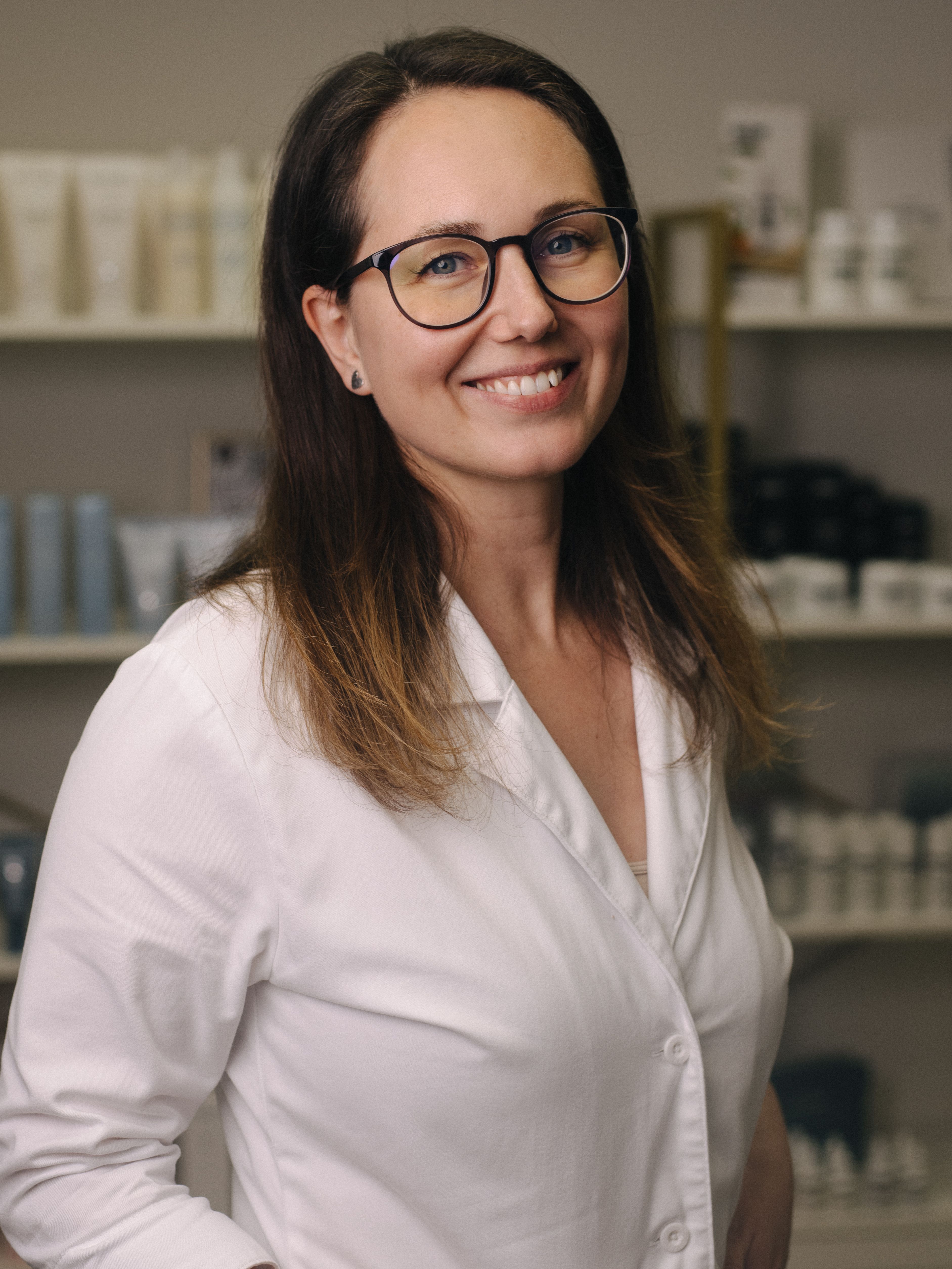 A smiling woman in a white lab coat and glasses stands in a salon waiting room
