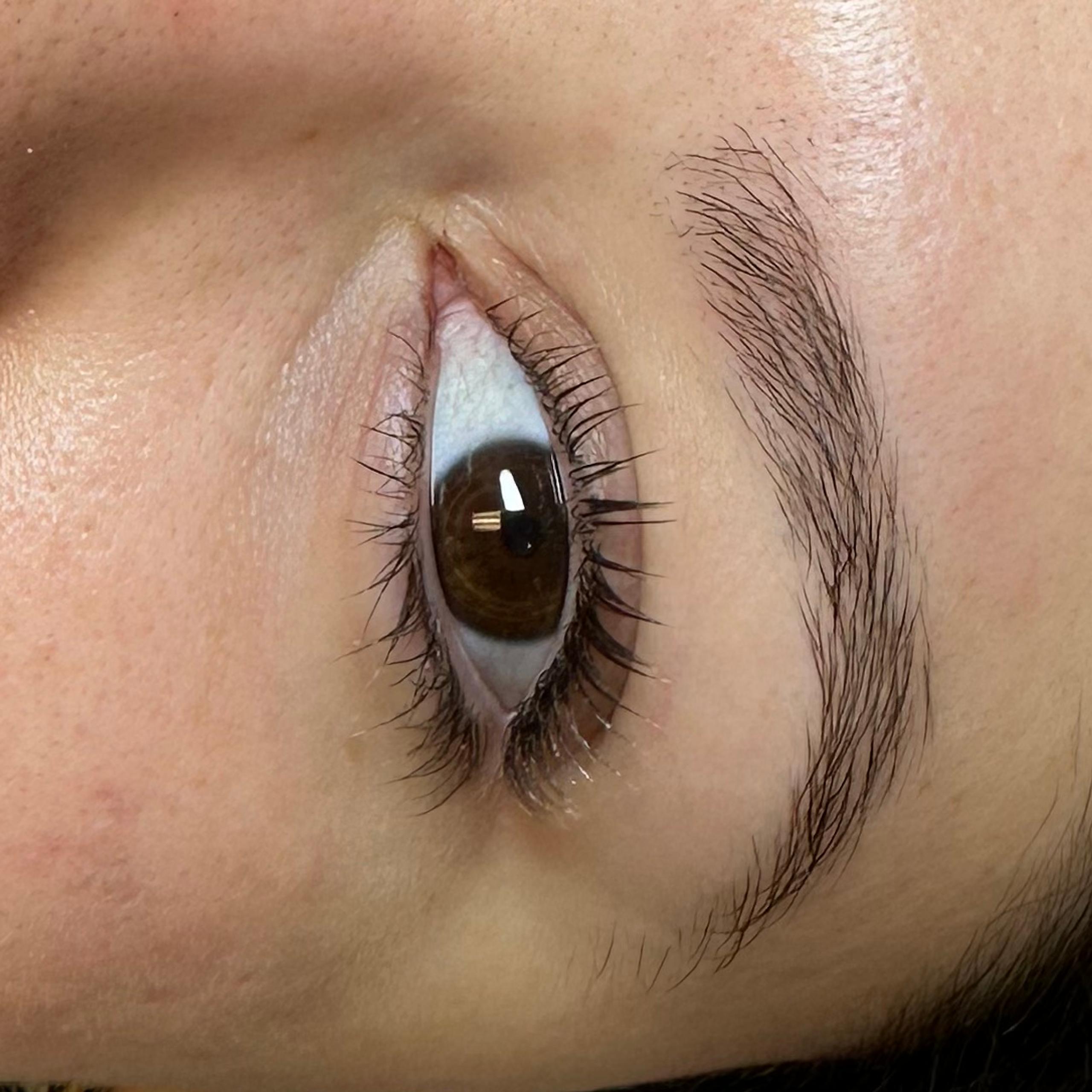 A woman looking at the camera, showing off lifted eyelashes with beauty tools beside her.