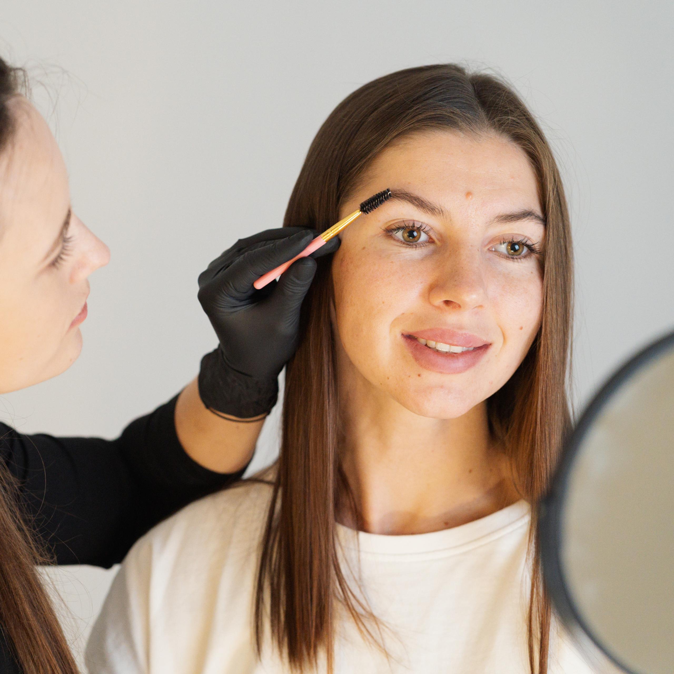 A brow artist brushes a woman's eyebrows.
