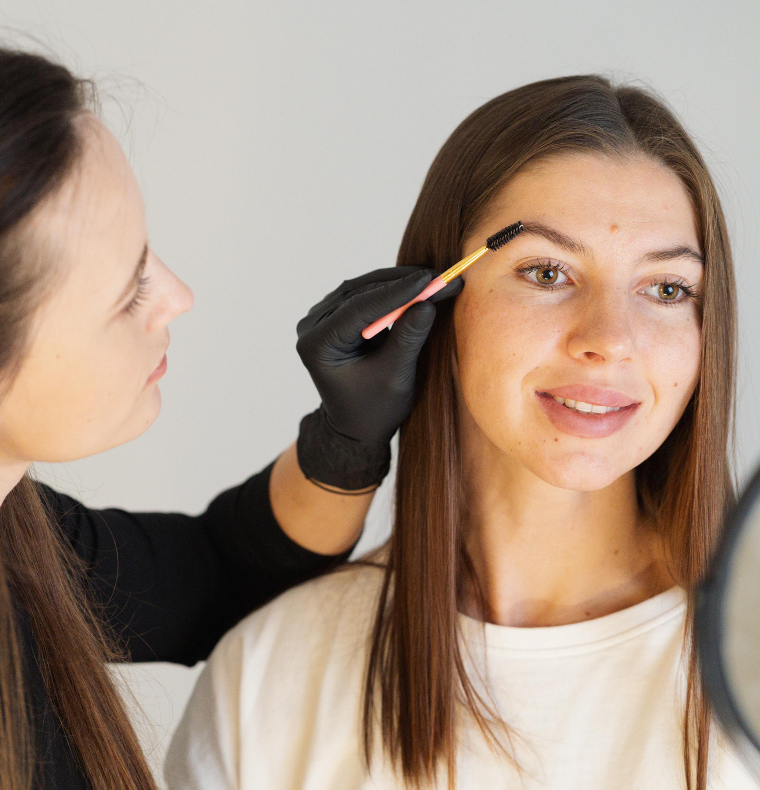 A woman styles another woman's eyebrow with a brush.