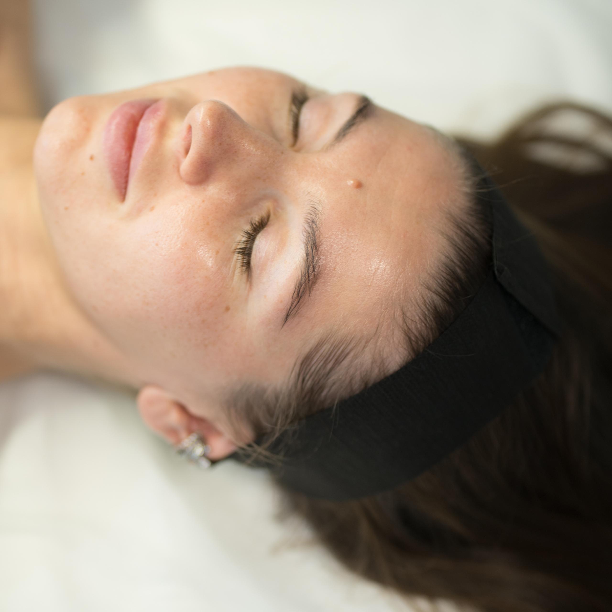 Woman with a black headband lies with closed eyes and soft smile