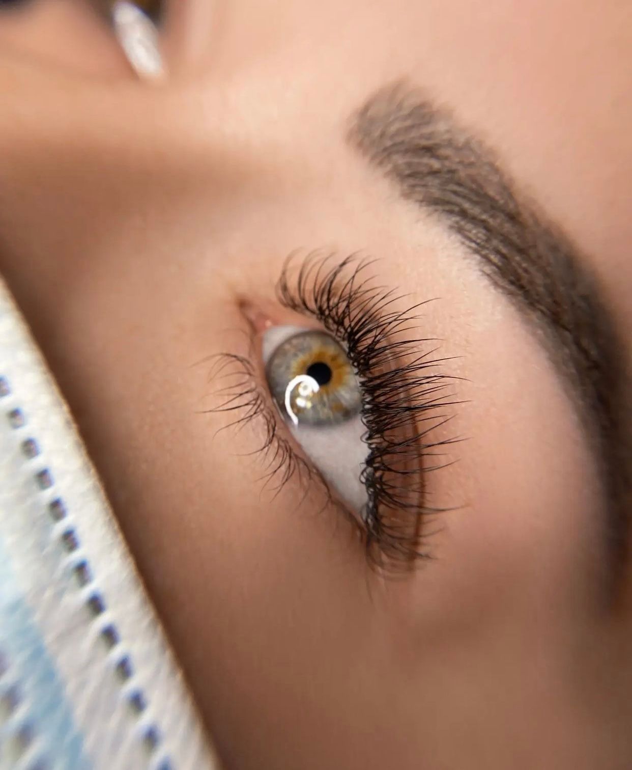 Close-up of a hazel eye with long, dark lash extensions looking upwards.