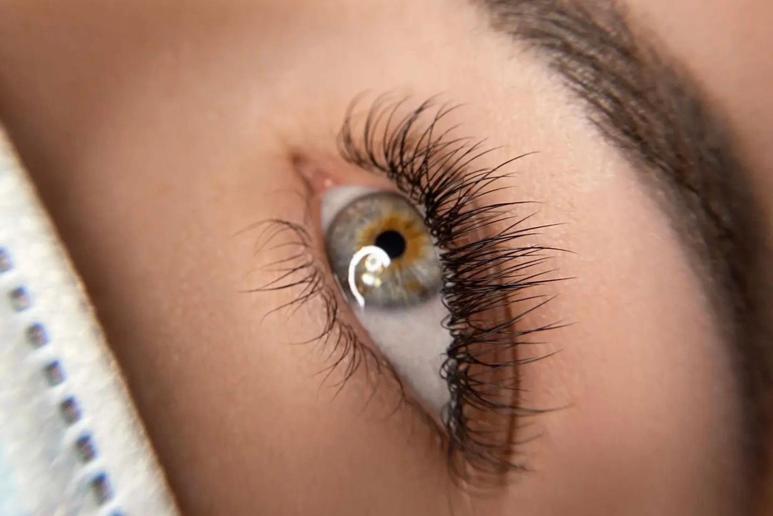 Close-up of a hazel eye with long, dark lash extensions looking upwards.