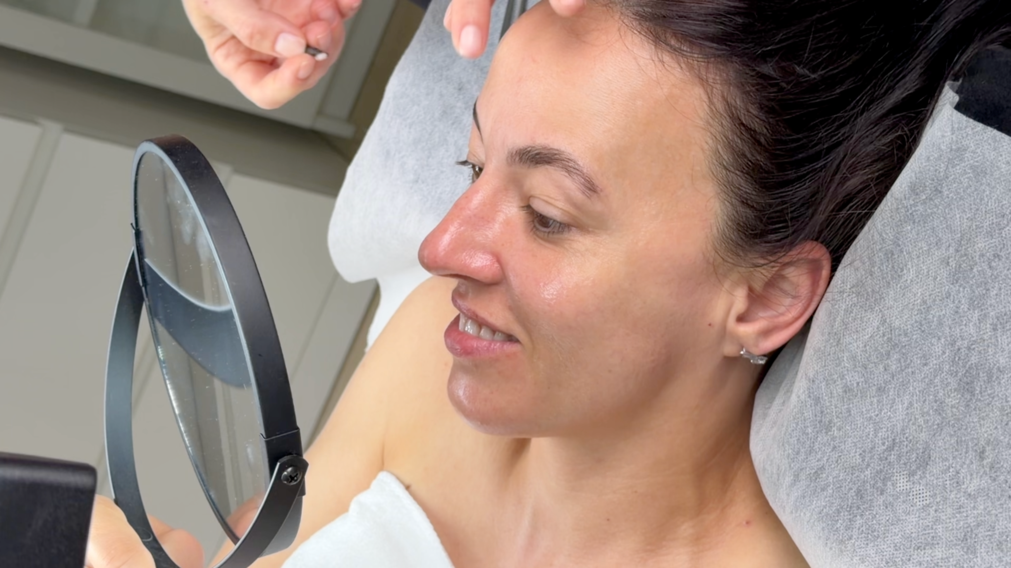 
Claude responded: Client on facial bed inspecting glowing post-treatment skin and laminated brushed-up brows in handheld mirror, esthetician's hands working above.
Client on facial bed inspecting glowing post-treatment skin and laminated brushed-up brows in handheld mirror, esthetician's hands working above.