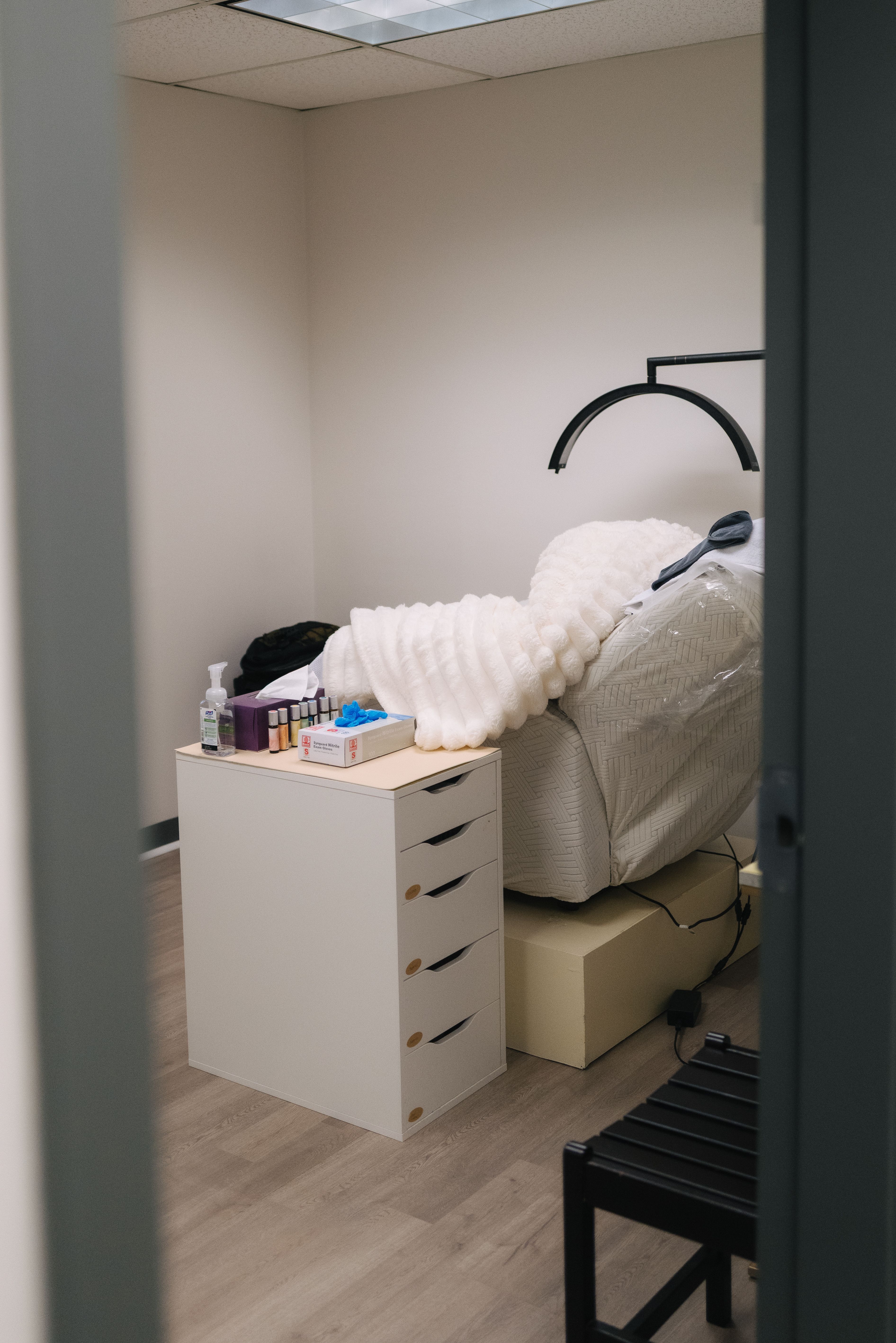 View through the doorway of a private treatment room with a reclining chair, white blanket, and overhead lamp.