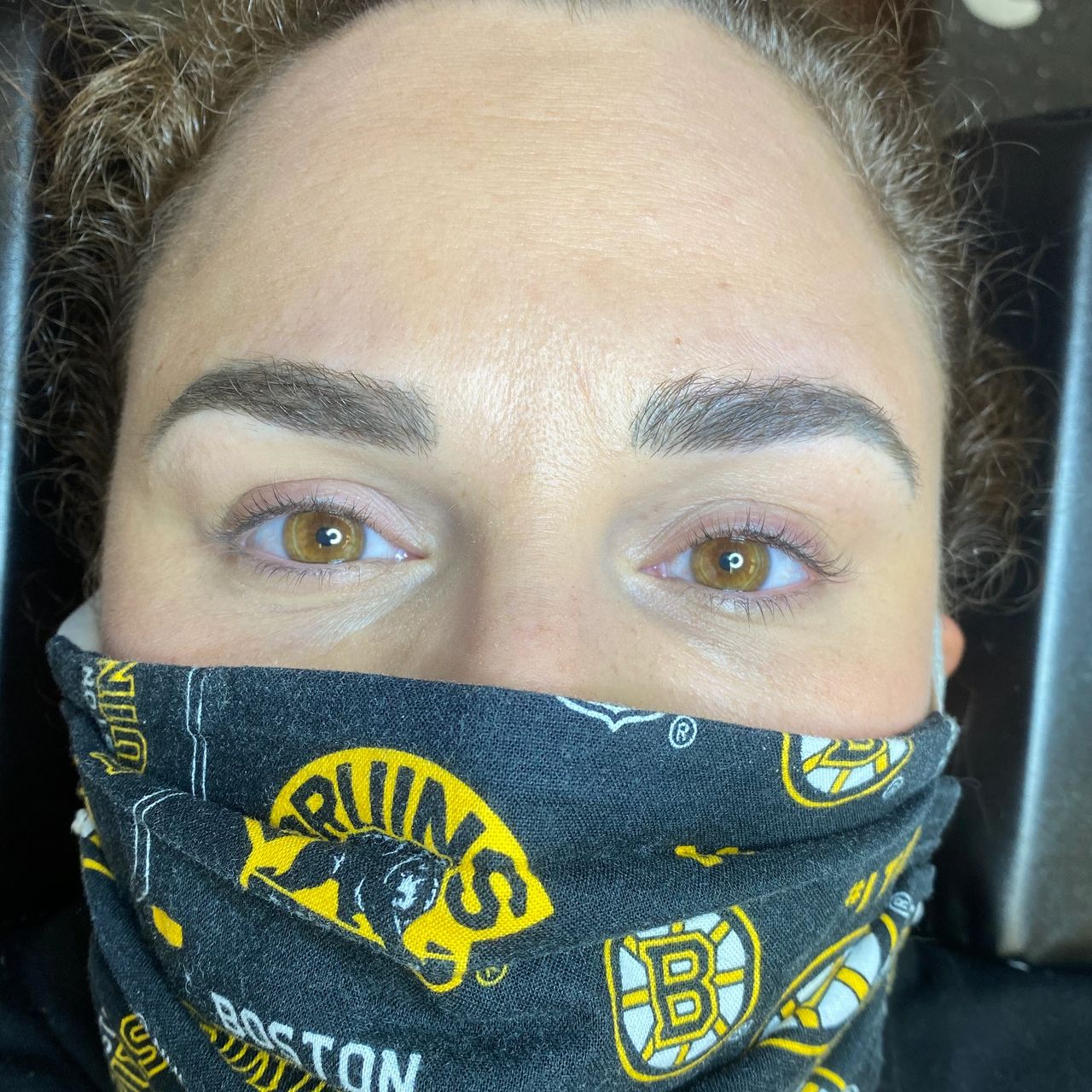 A person with light brown eyes and neatly shaped eyebrows looks up, wearing a black mask