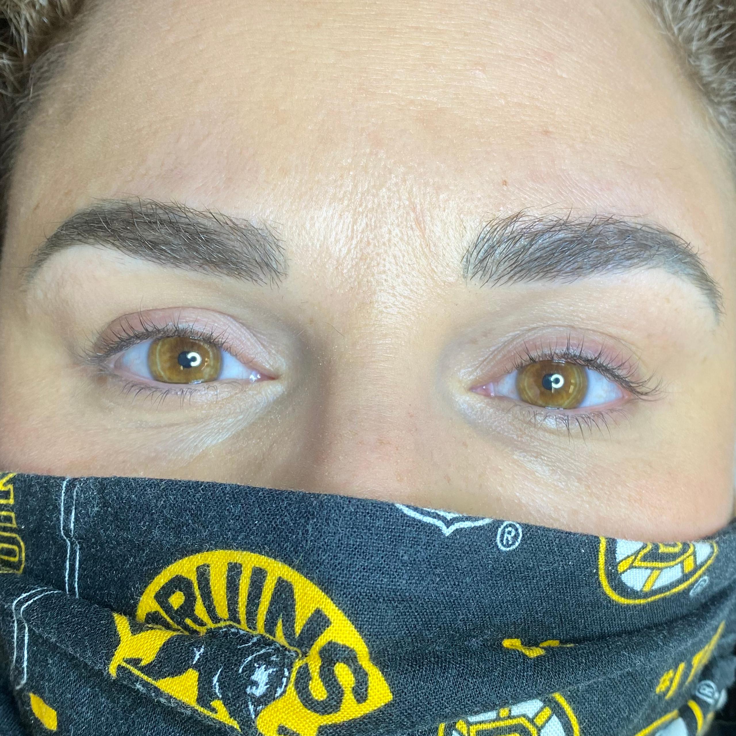 A person with light brown eyes and neatly shaped eyebrows looks up, wearing a black mask