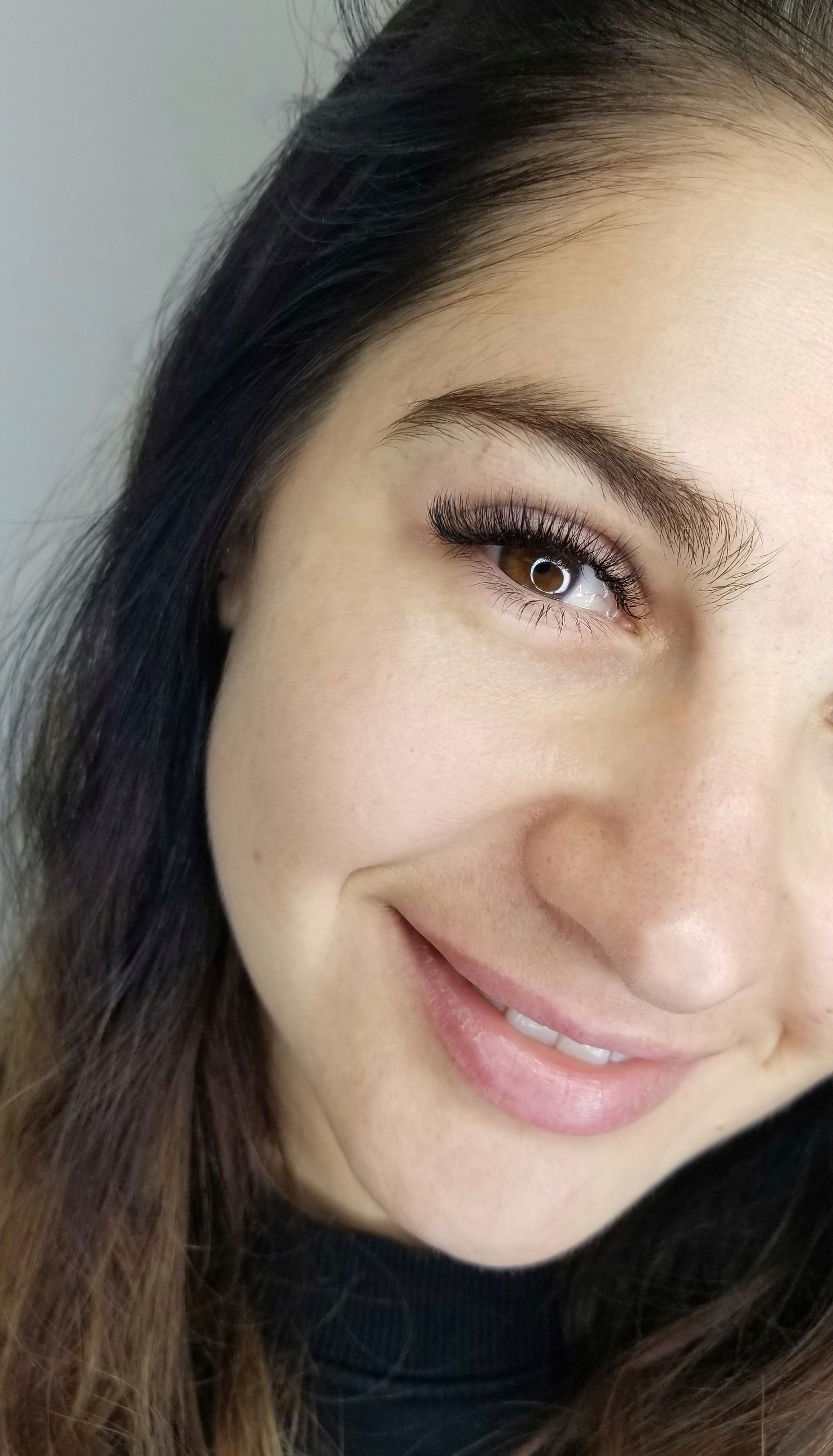 Close-up of a smiling woman showing one brown eye with long, voluminous eyelashes.