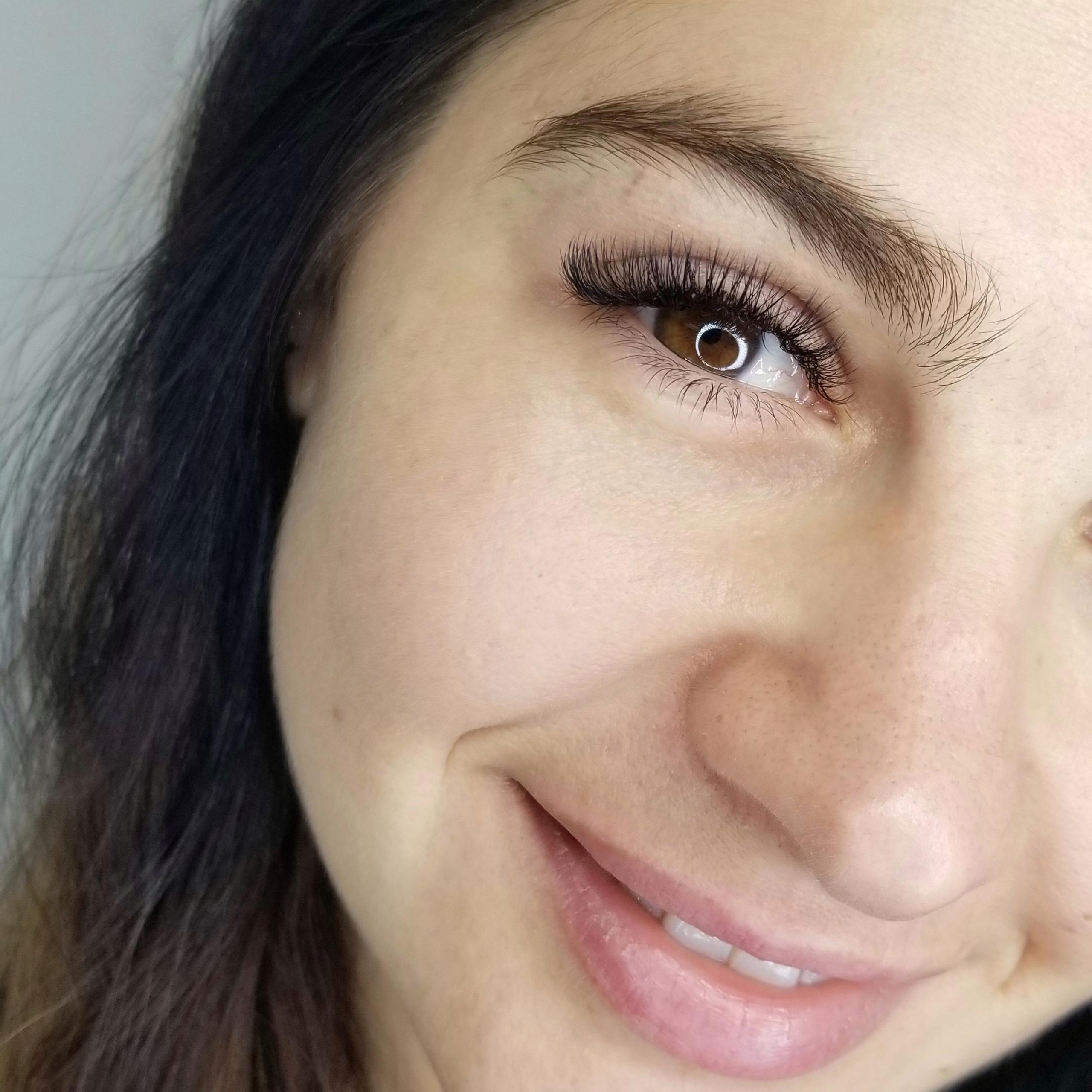 Close-up of a smiling woman showing one brown eye with long, voluminous eyelashes.