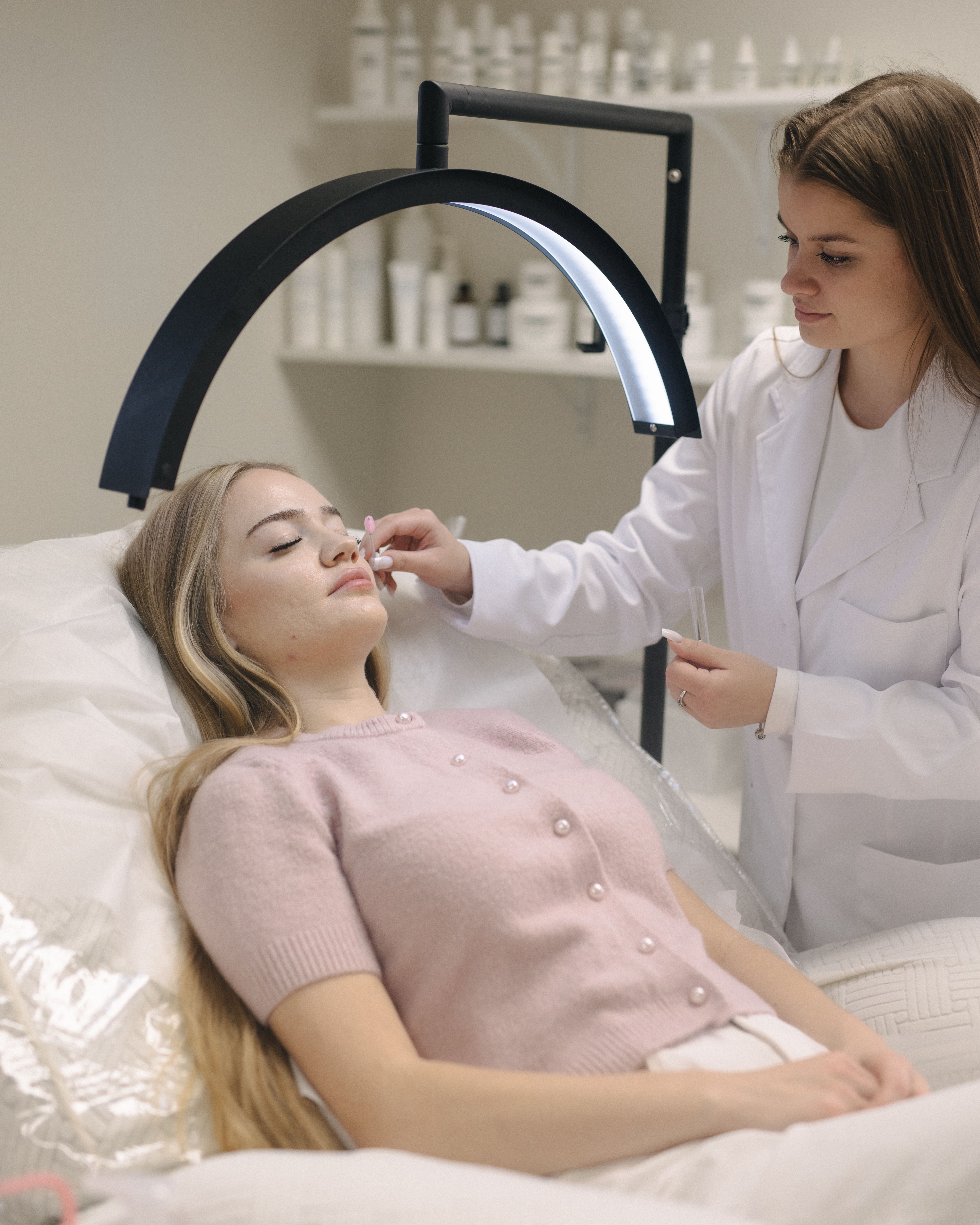 An esthetician brushes client's lashes under a bright ring lamp.