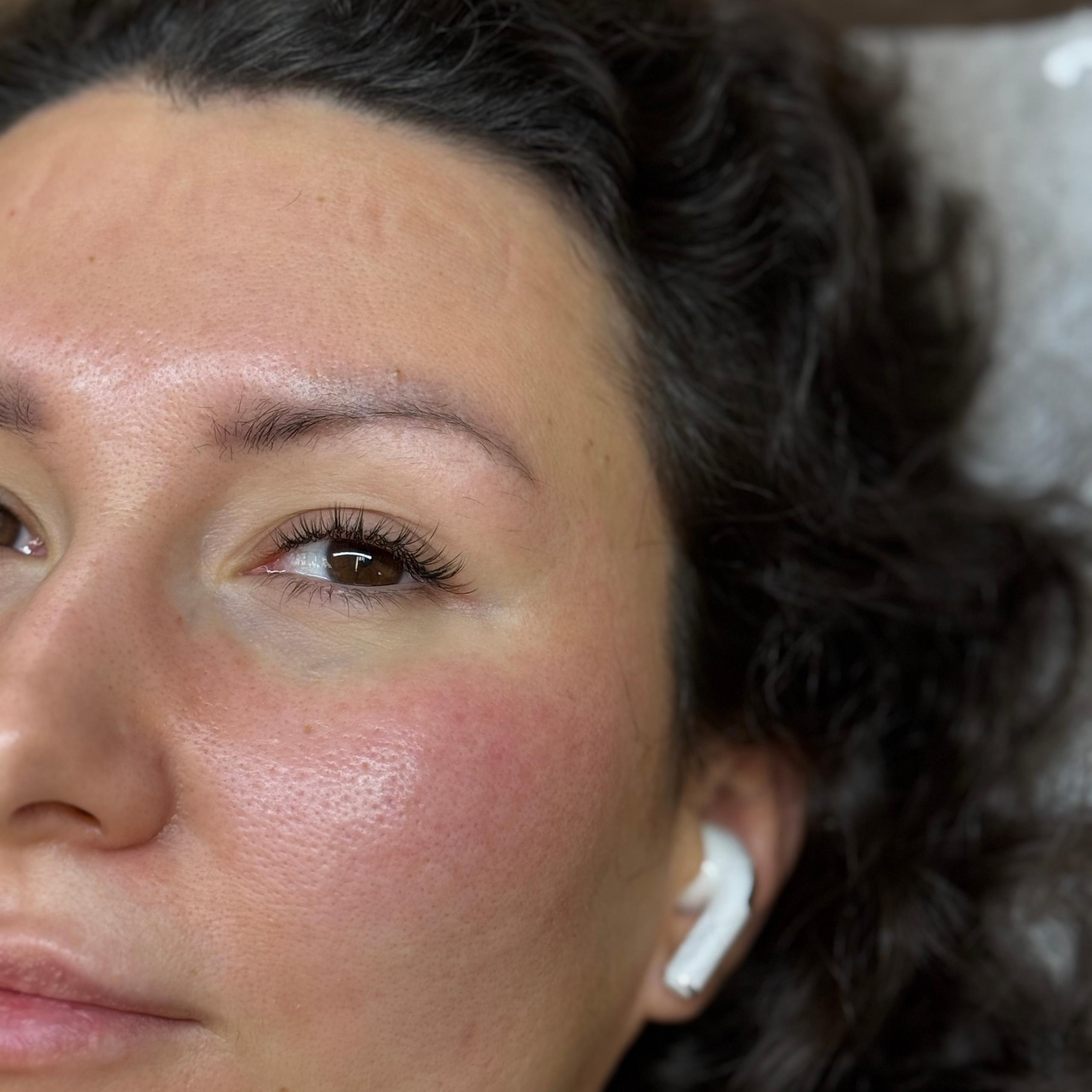 Close-up of a person's right eye with short and curly lash extensions wearing a white earbud.