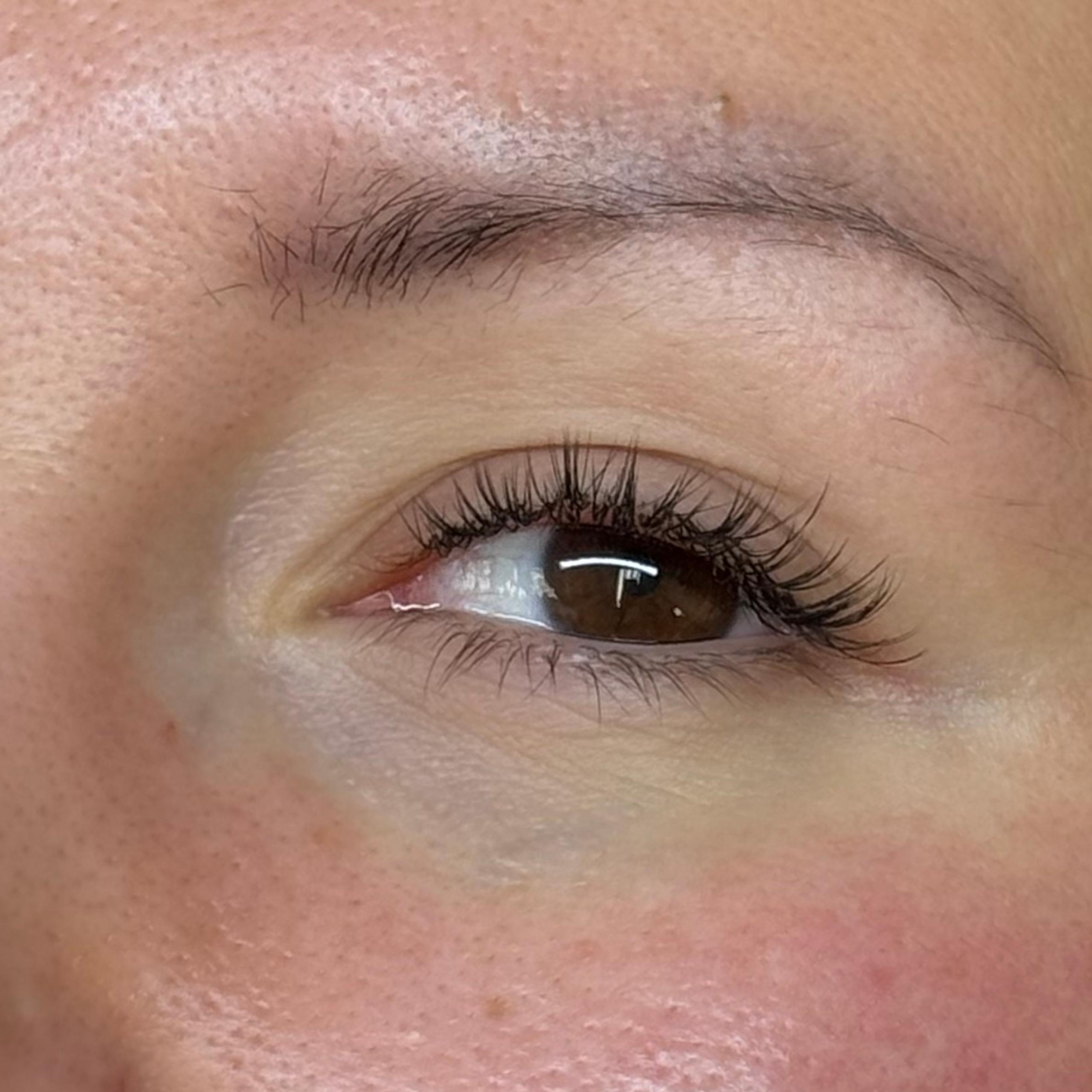 Close-up of a person's right eye with short and curly lash extensions wearing a white earbud.