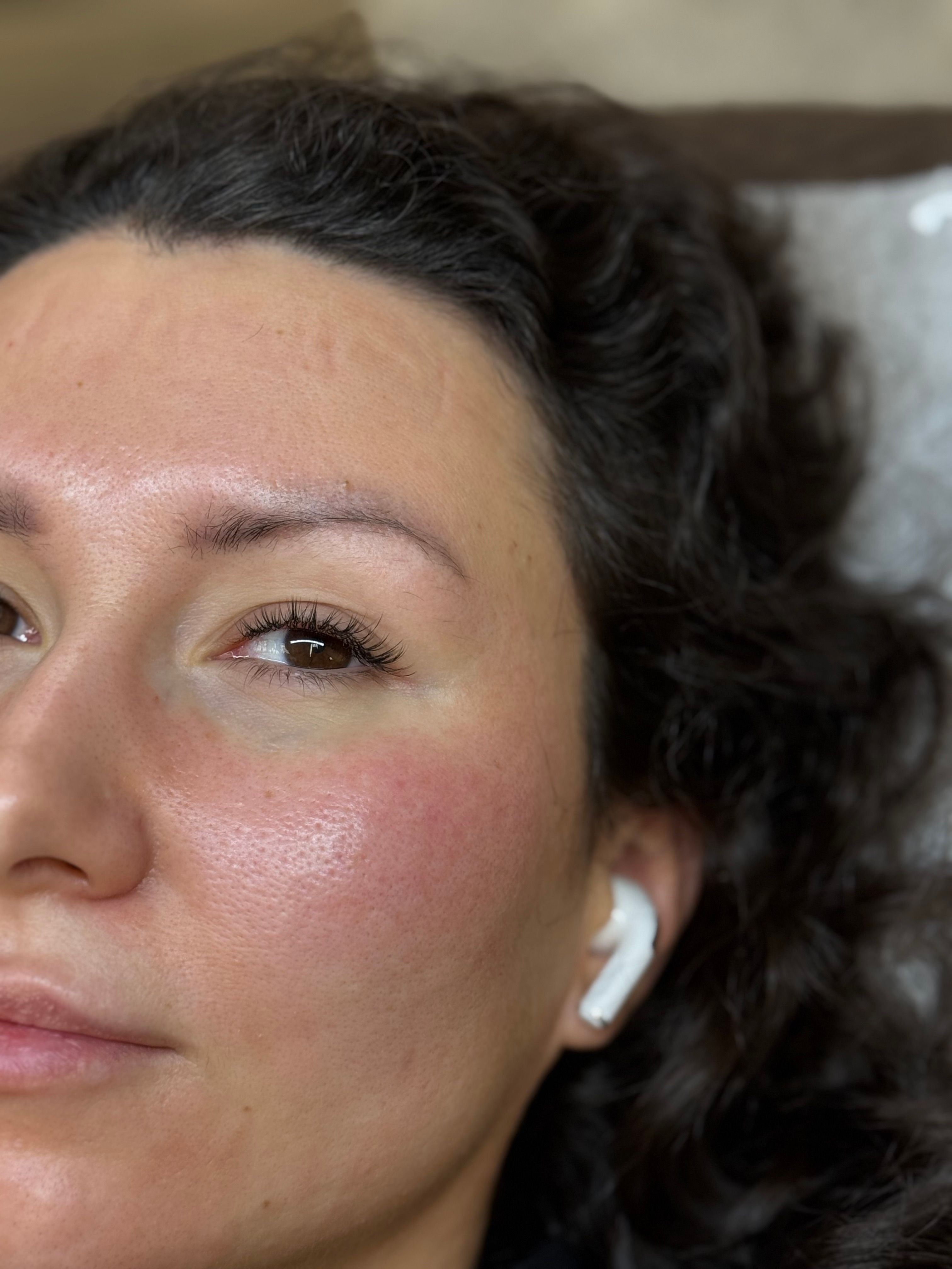 Close-up of the right side of a woman's face with dark curly hair, an open eye with hybrid eyelash extensions