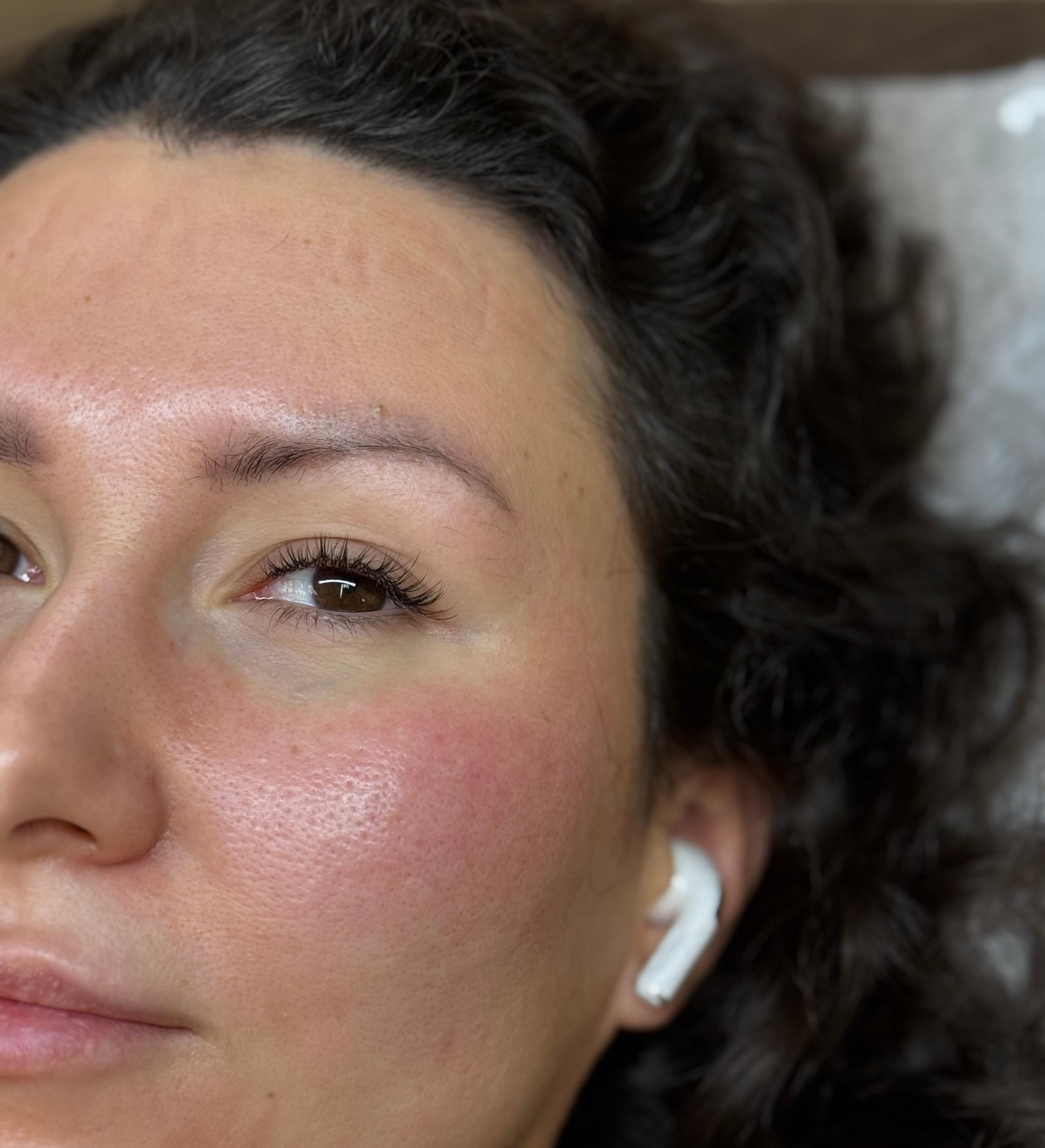 Close-up of the right side of a woman's face with dark curly hair, an open eye with hybrid eyelash extensions