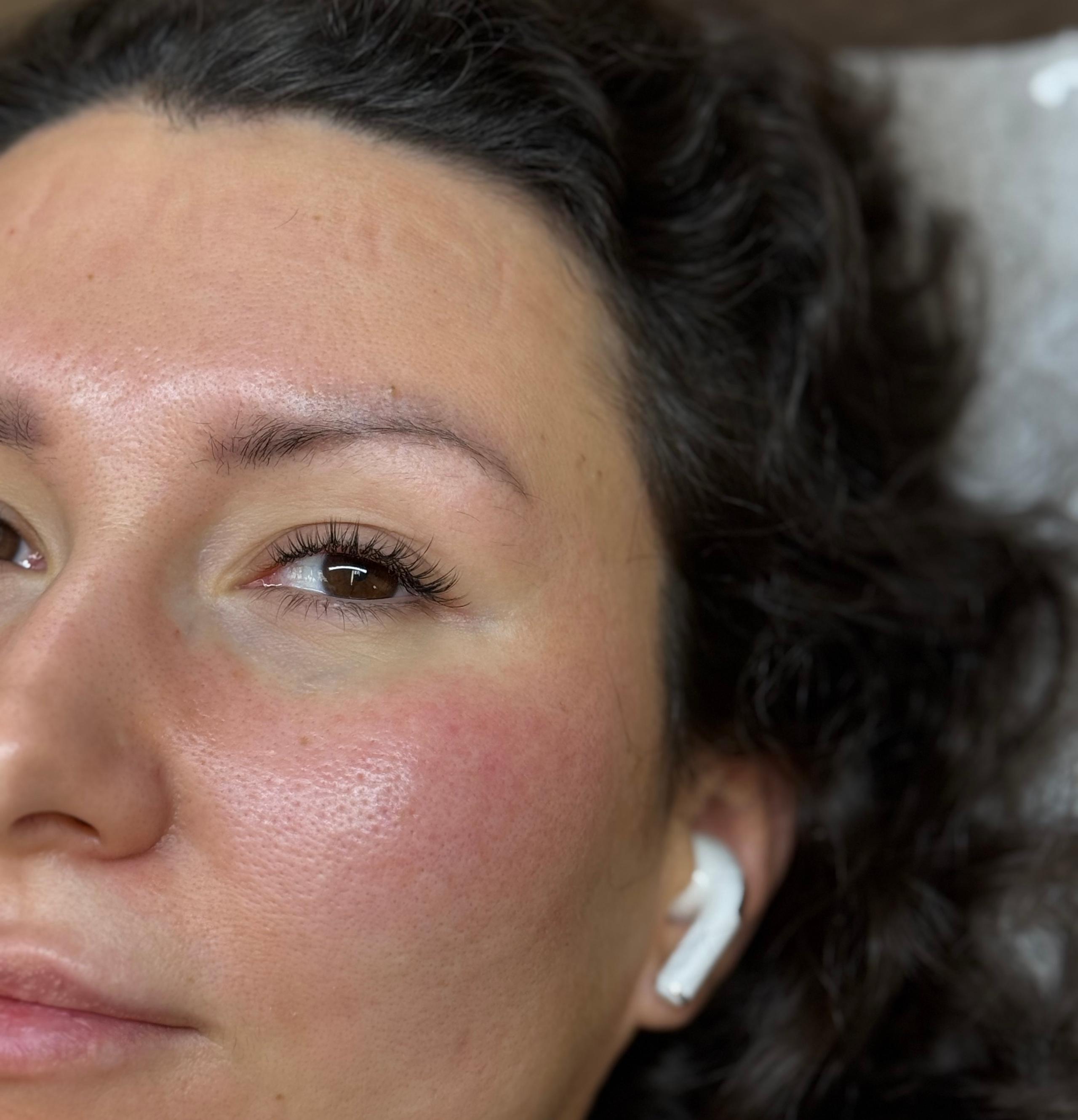 Close-up of the right side of a woman's face with dark curly hair, an open eye with hybrid eyelash extensions