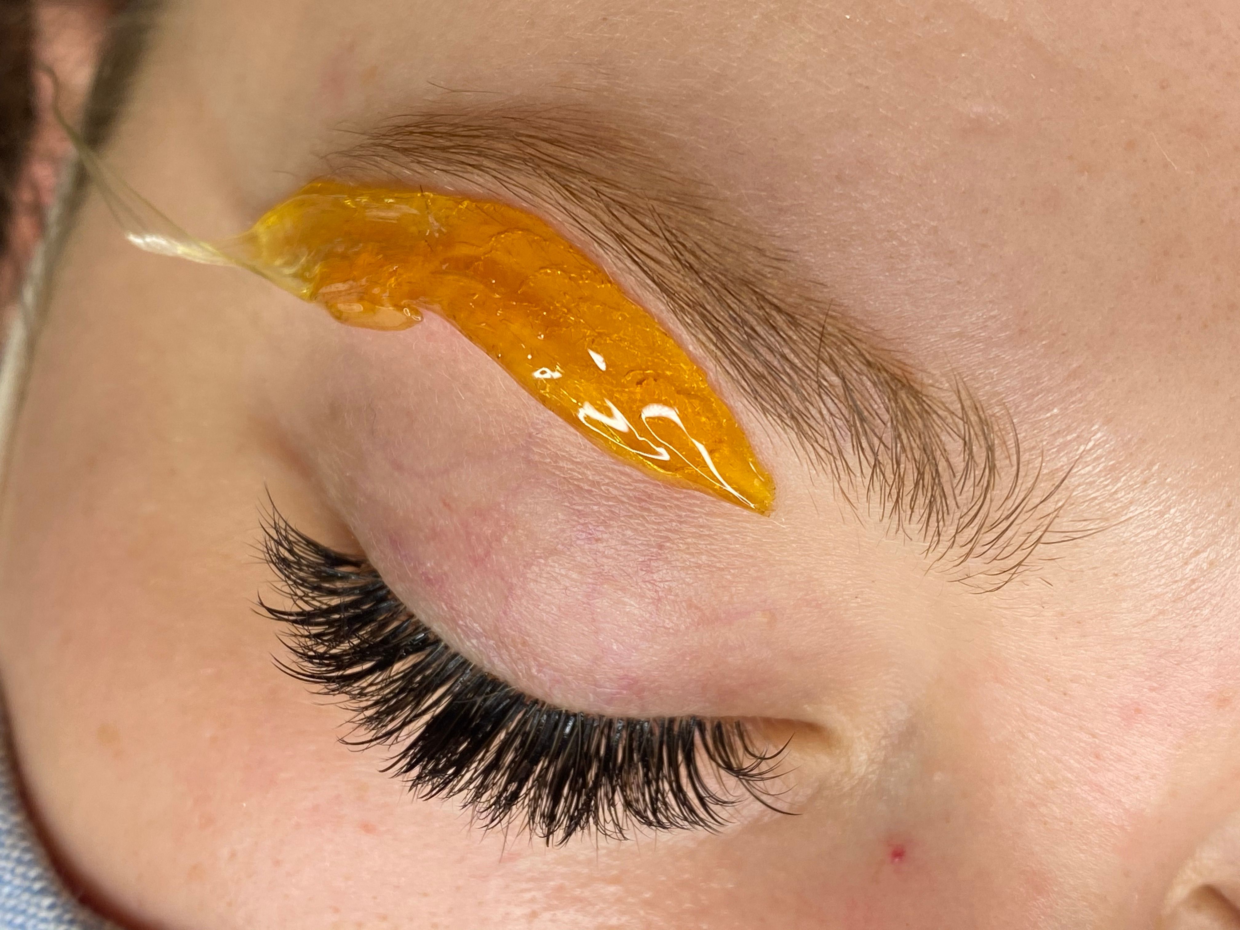 Close-up of an eyebrow being waxed with amber paste