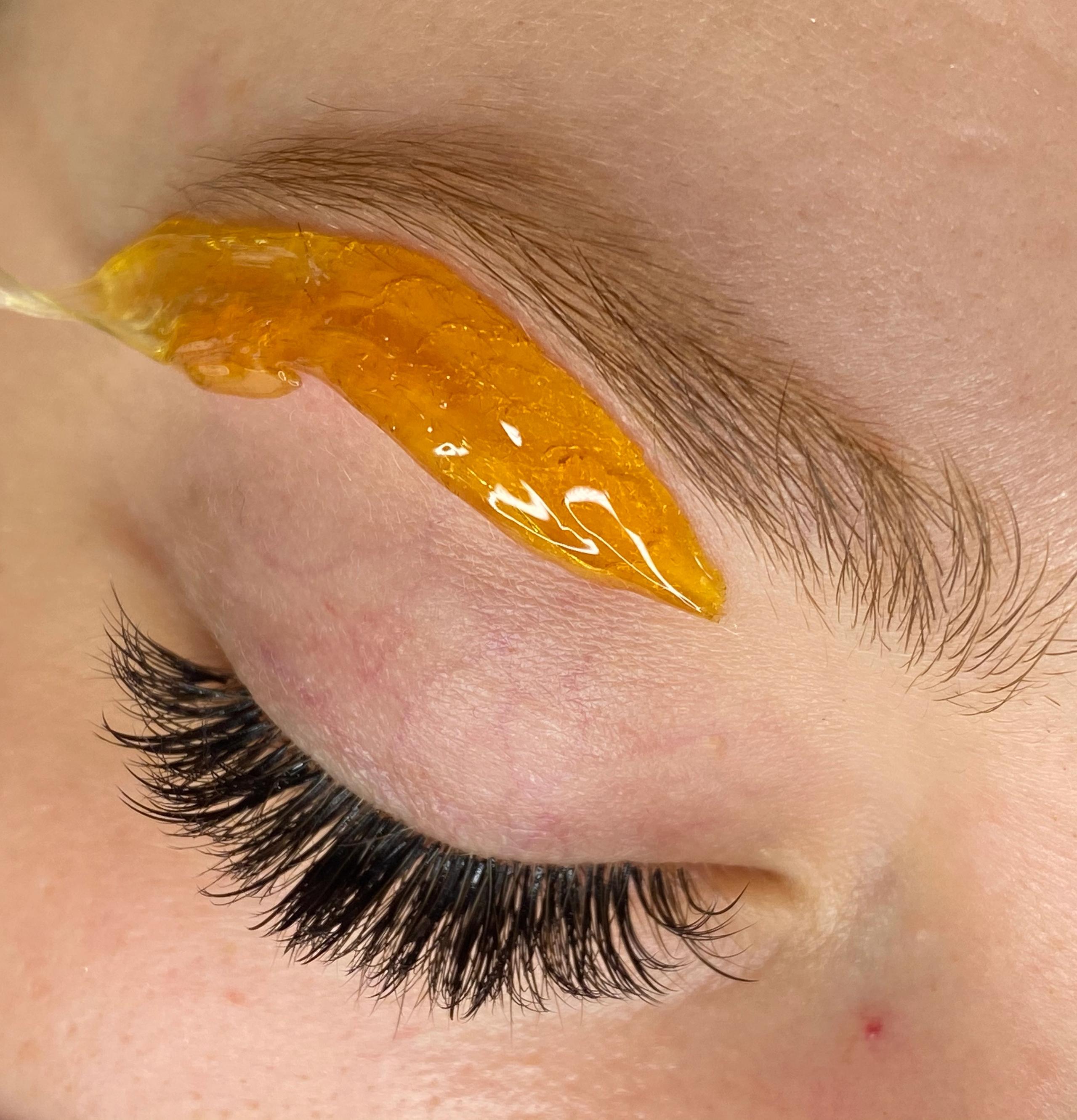Close-up of an eyebrow being waxed with amber paste