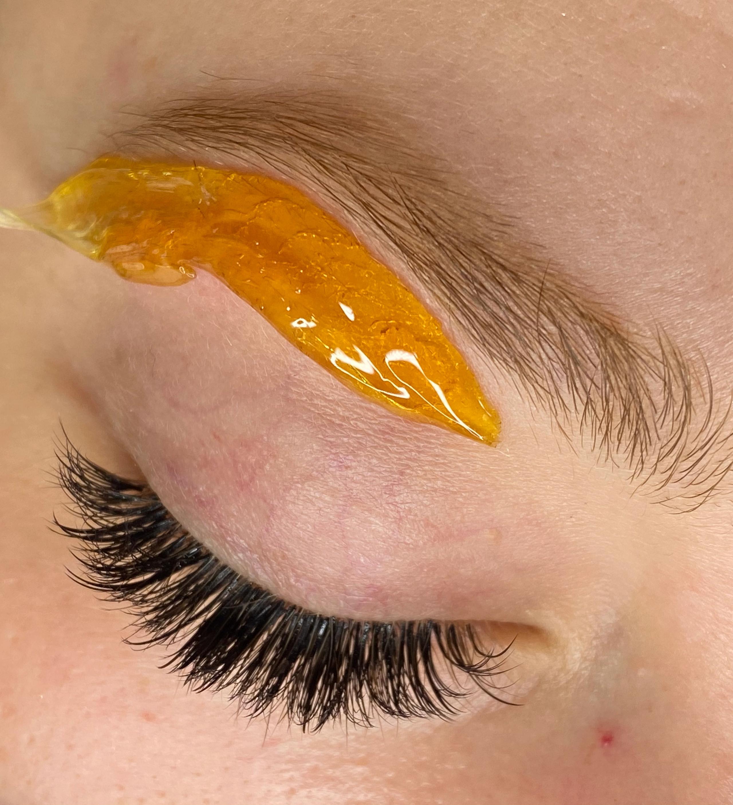 Close-up of an eyebrow being waxed with amber paste