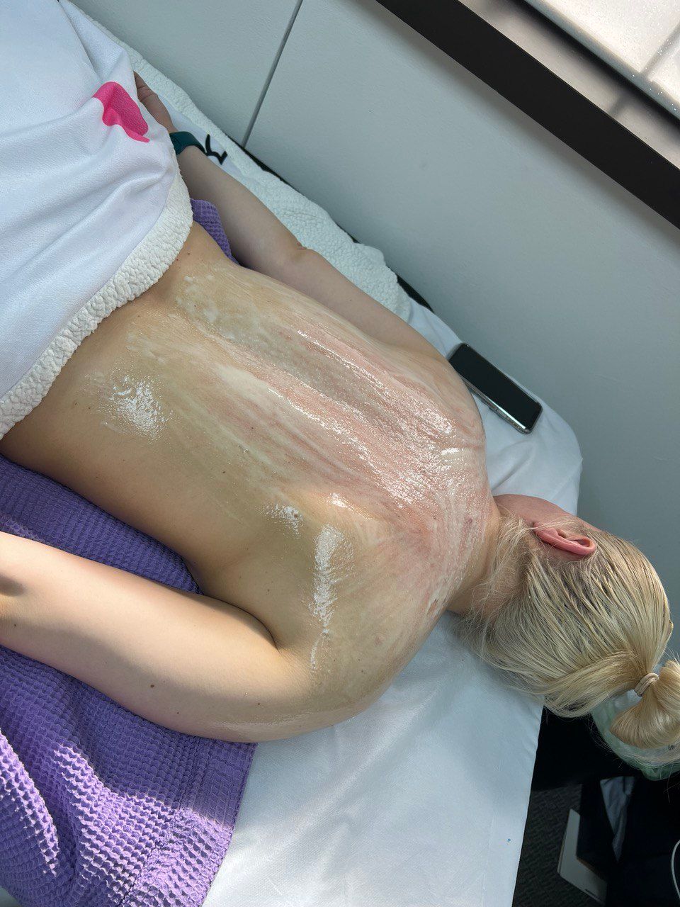 A person lying face down on a treatment table, with their back covered in a creamy mask