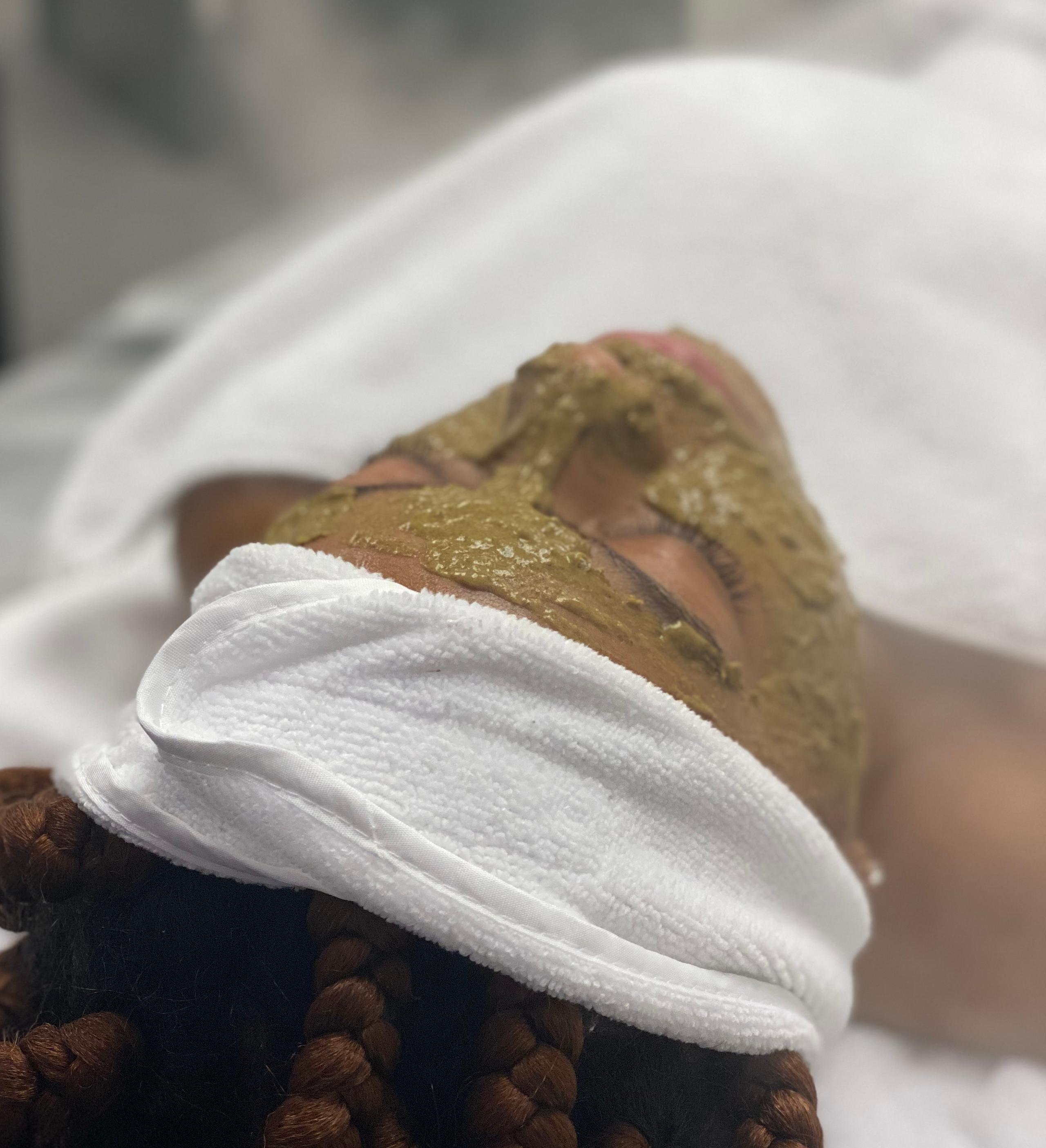 Person with a green face mask and white headband at a spa.