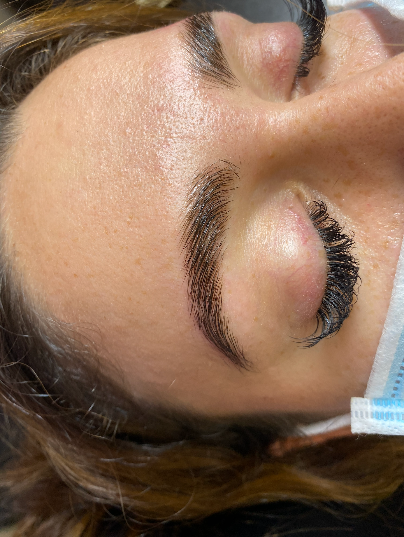 Close-up of a person's face with eyes closed, featuring shiny, upward-styled eyebrows