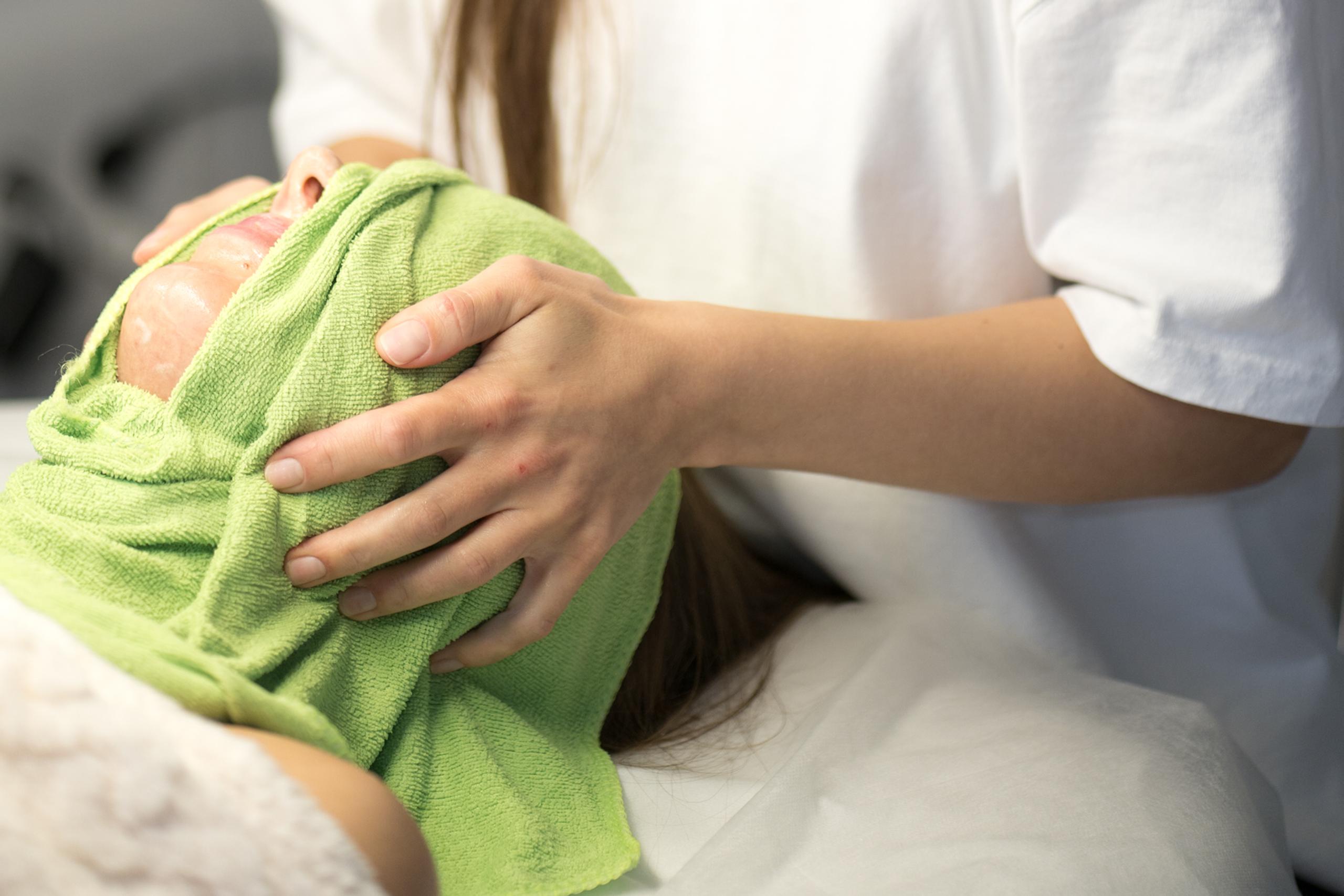 Beauty professional gently covering a client's face with a green towel.