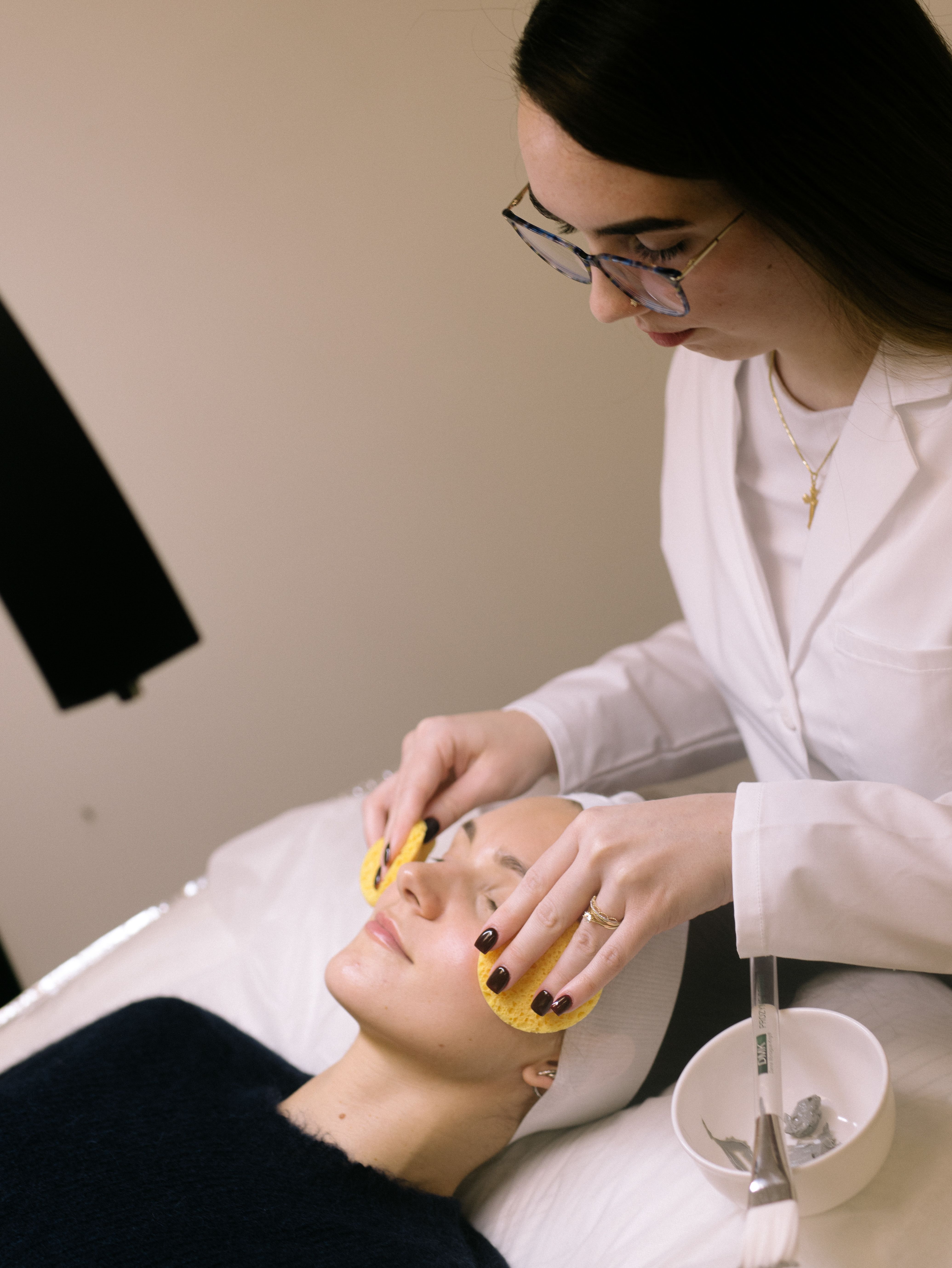 Esthetician cleansing a client’s face with sponges at the start of a facial.