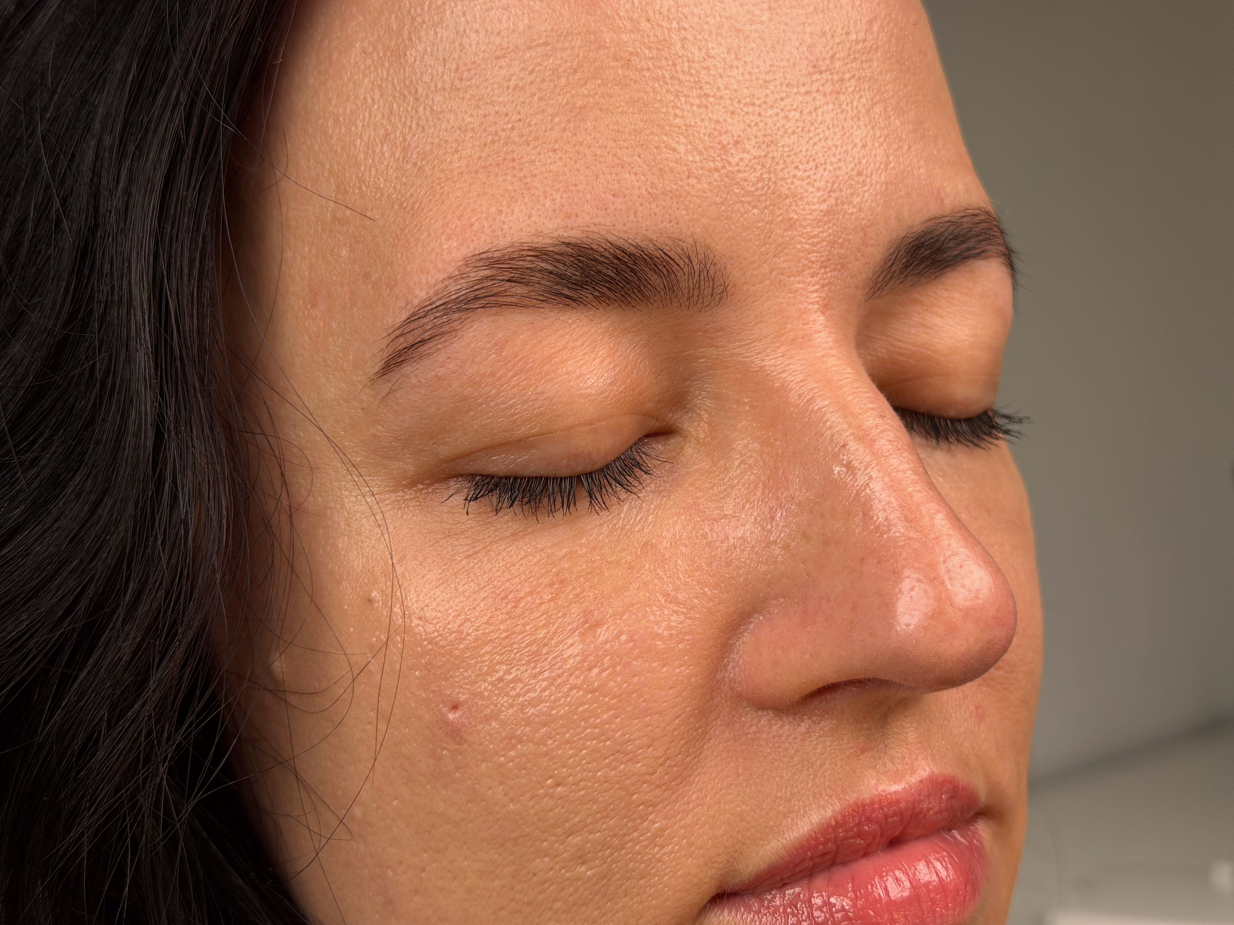Close up of a woman's face with closed eyes and relaxed smile featuring freshly styled and tinted dark brown eyebrows
