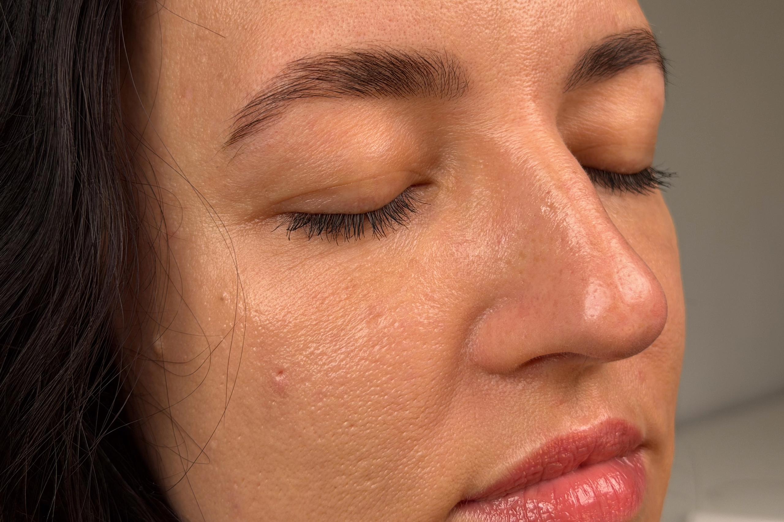 Close up of a woman's face with closed eyes and relaxed smile featuring freshly styled and tinted dark brown eyebrows
