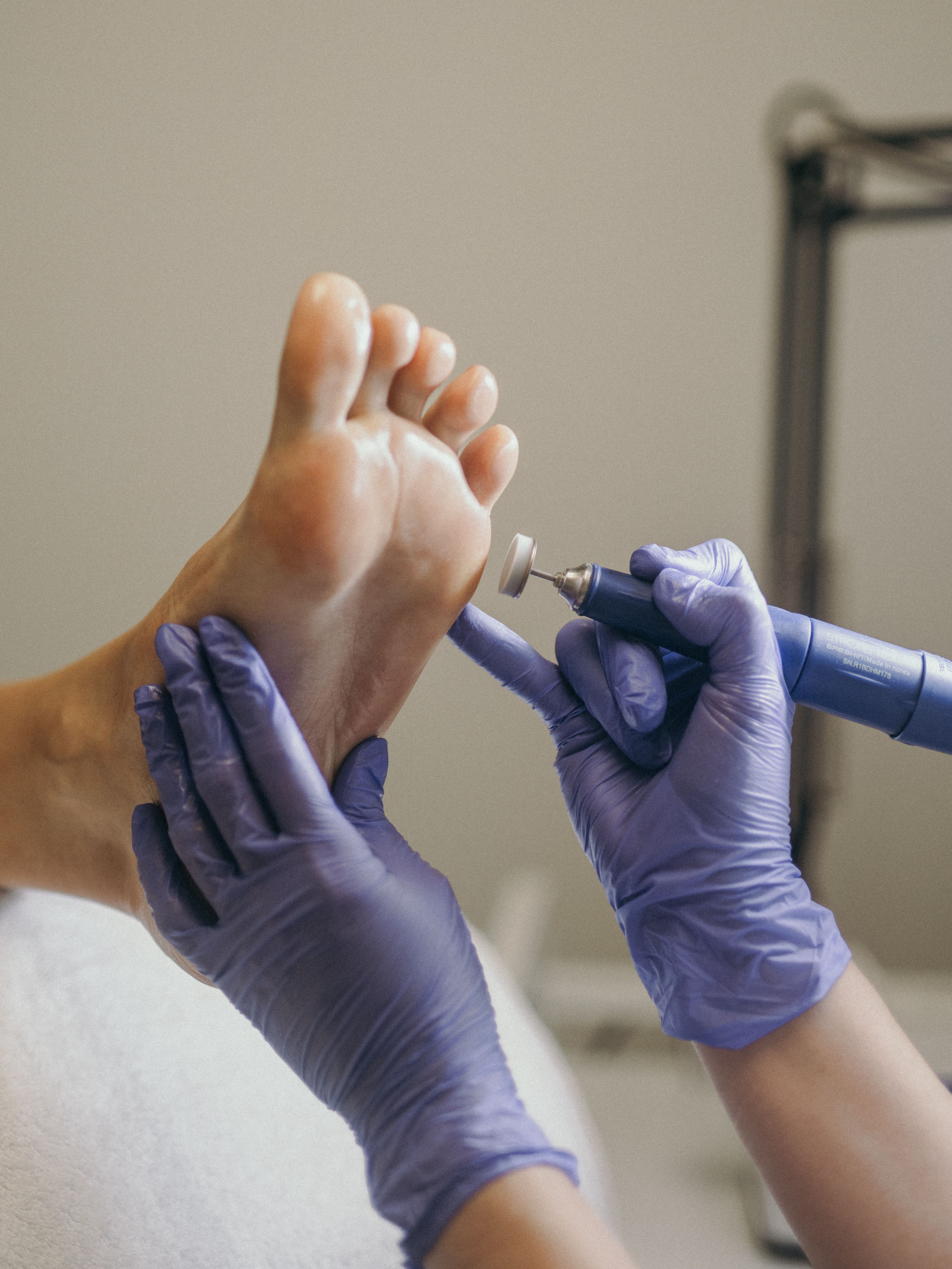 Gloved hands performing foot care with an electric file.