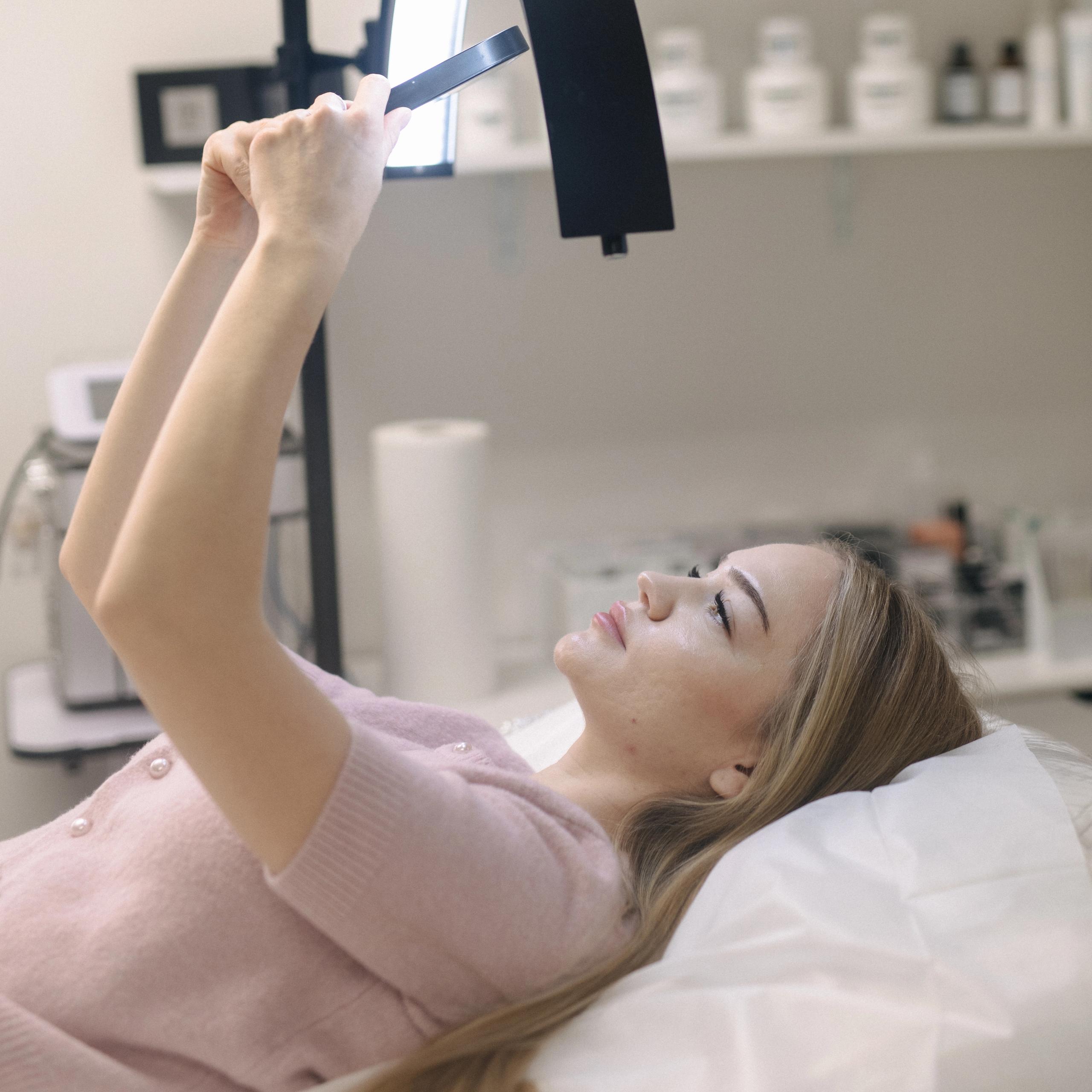 A woman lies on a treatment bed, looking at herself in the mirror