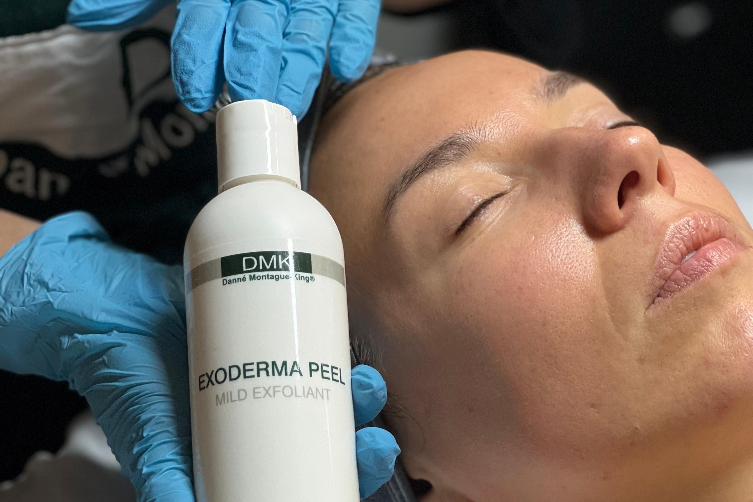 DMK Exoderma Peel mild exfoliant bottle held by gloved hands next to a person's face