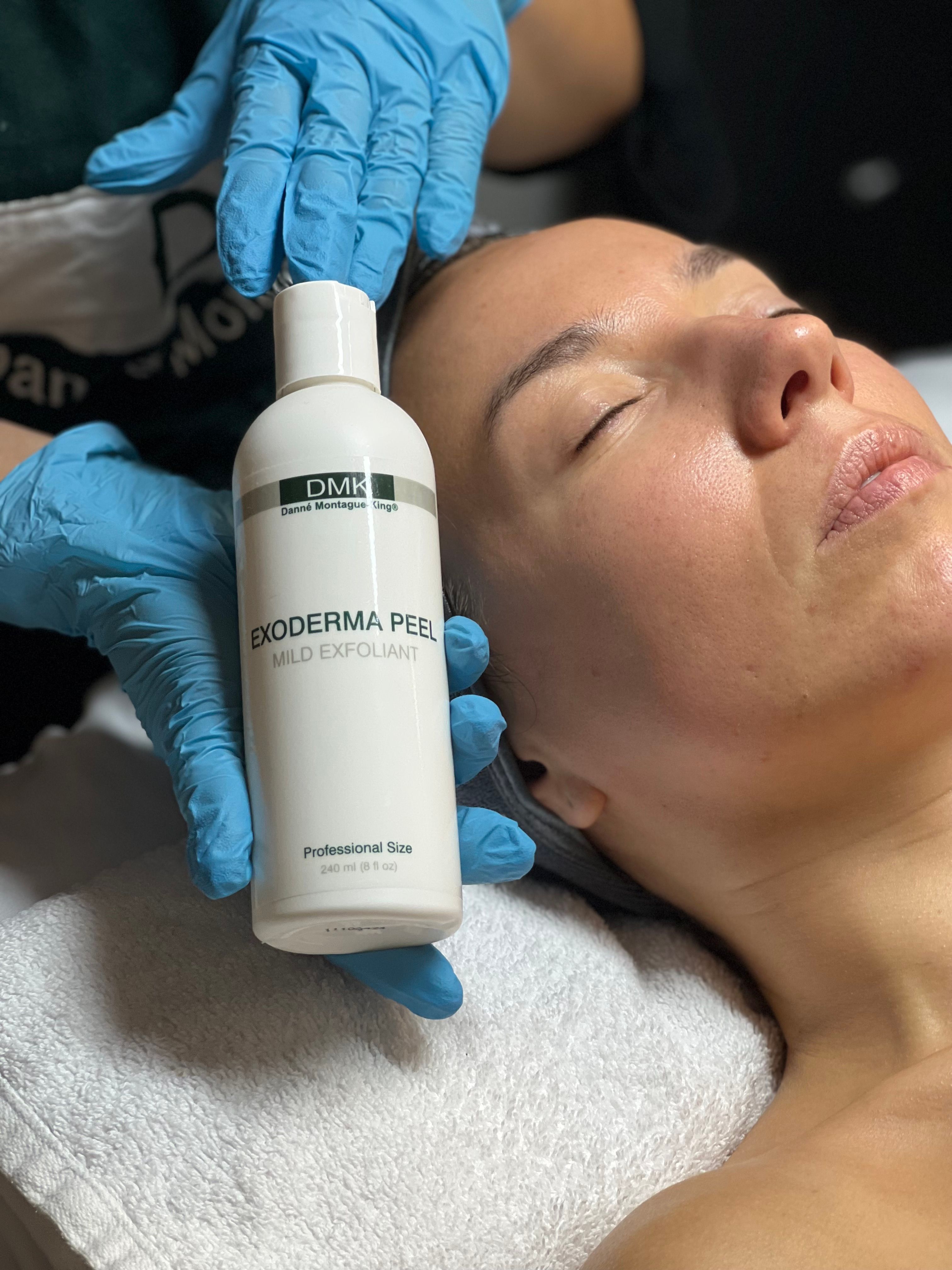 Gloved hands hold a DMK Exoderma Peel bottle next to a woman's face