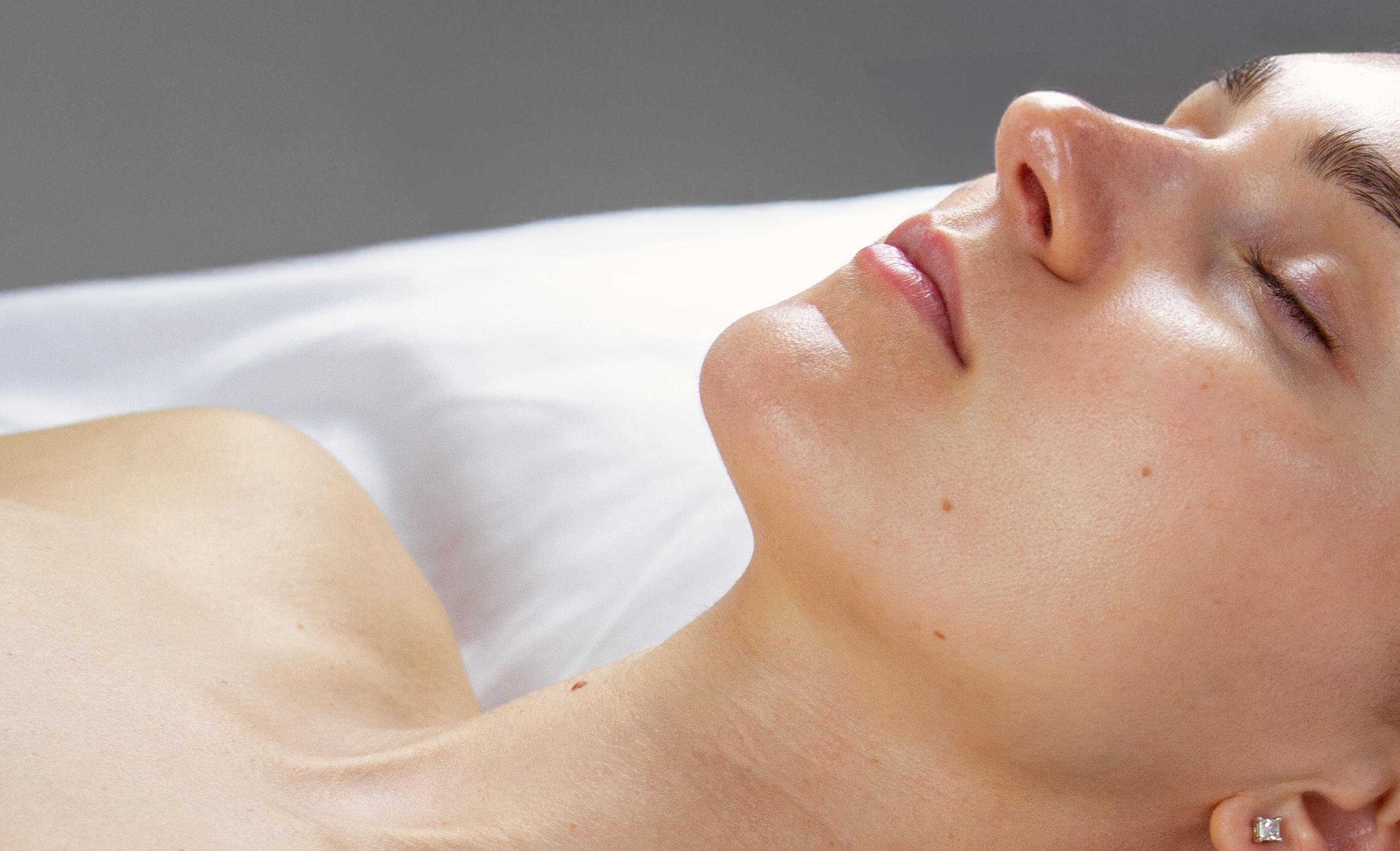 Close-up side profile of a person's jawline, neck, and upper chest.