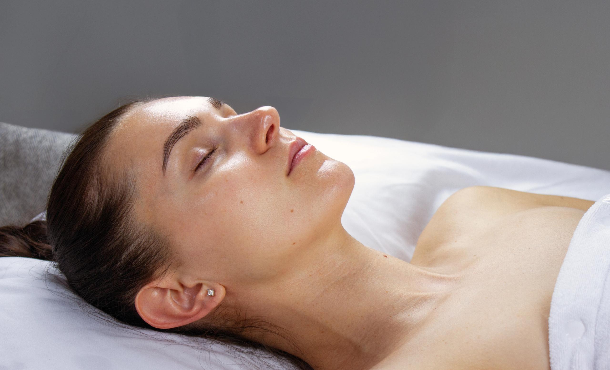 Woman with closed eyes relaxing on a white spa bed.