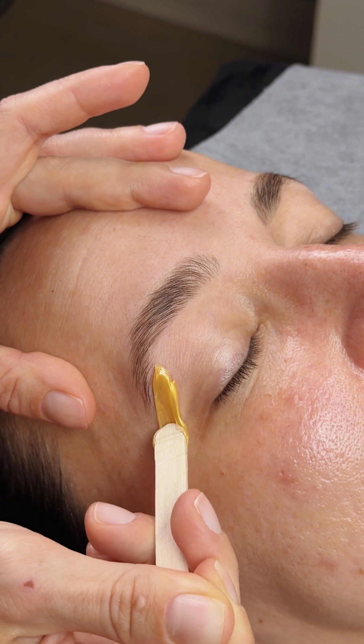A cosmetologist waxes a girl's eyebrows