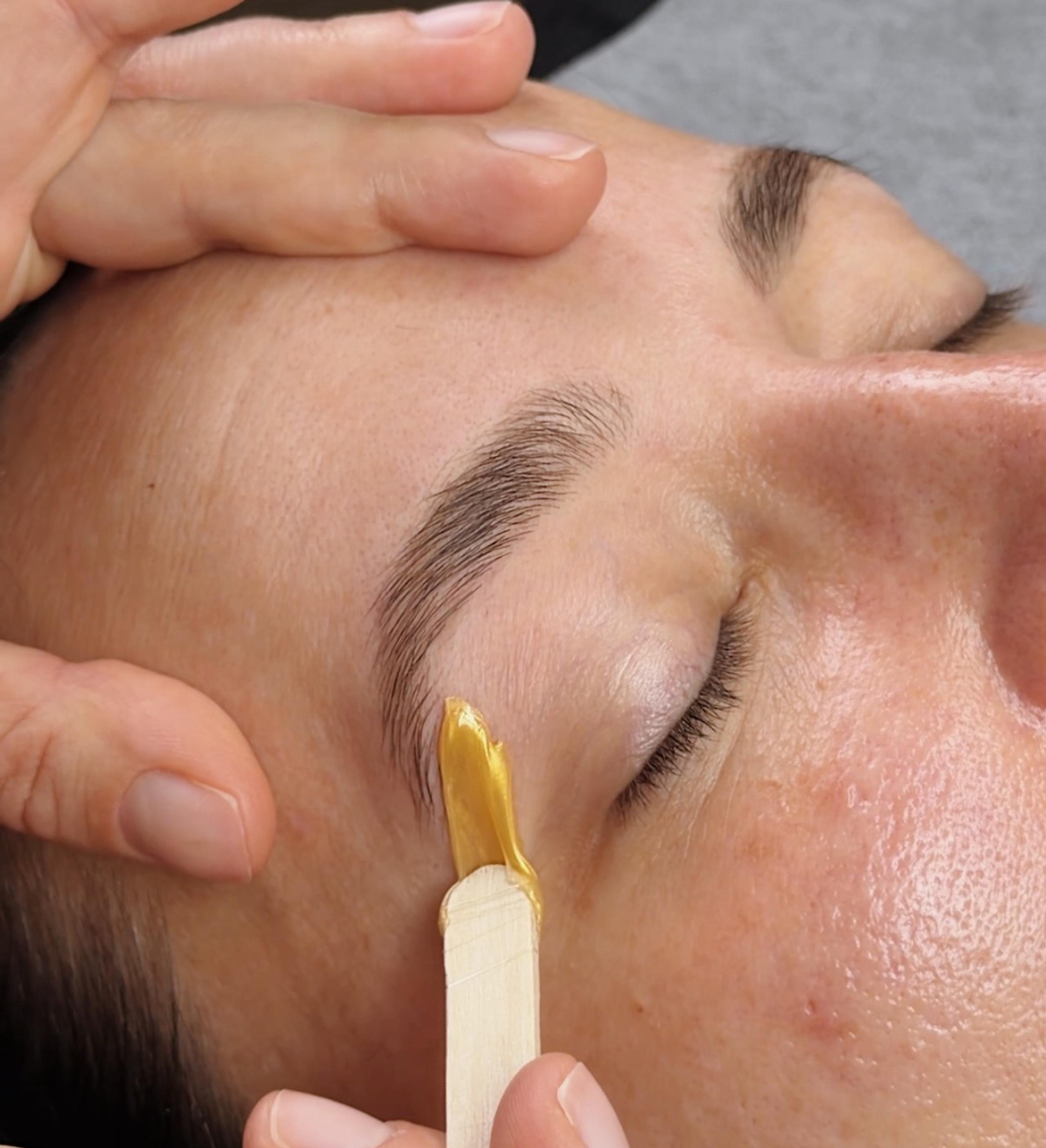 A cosmetologist waxes a girl's eyebrows