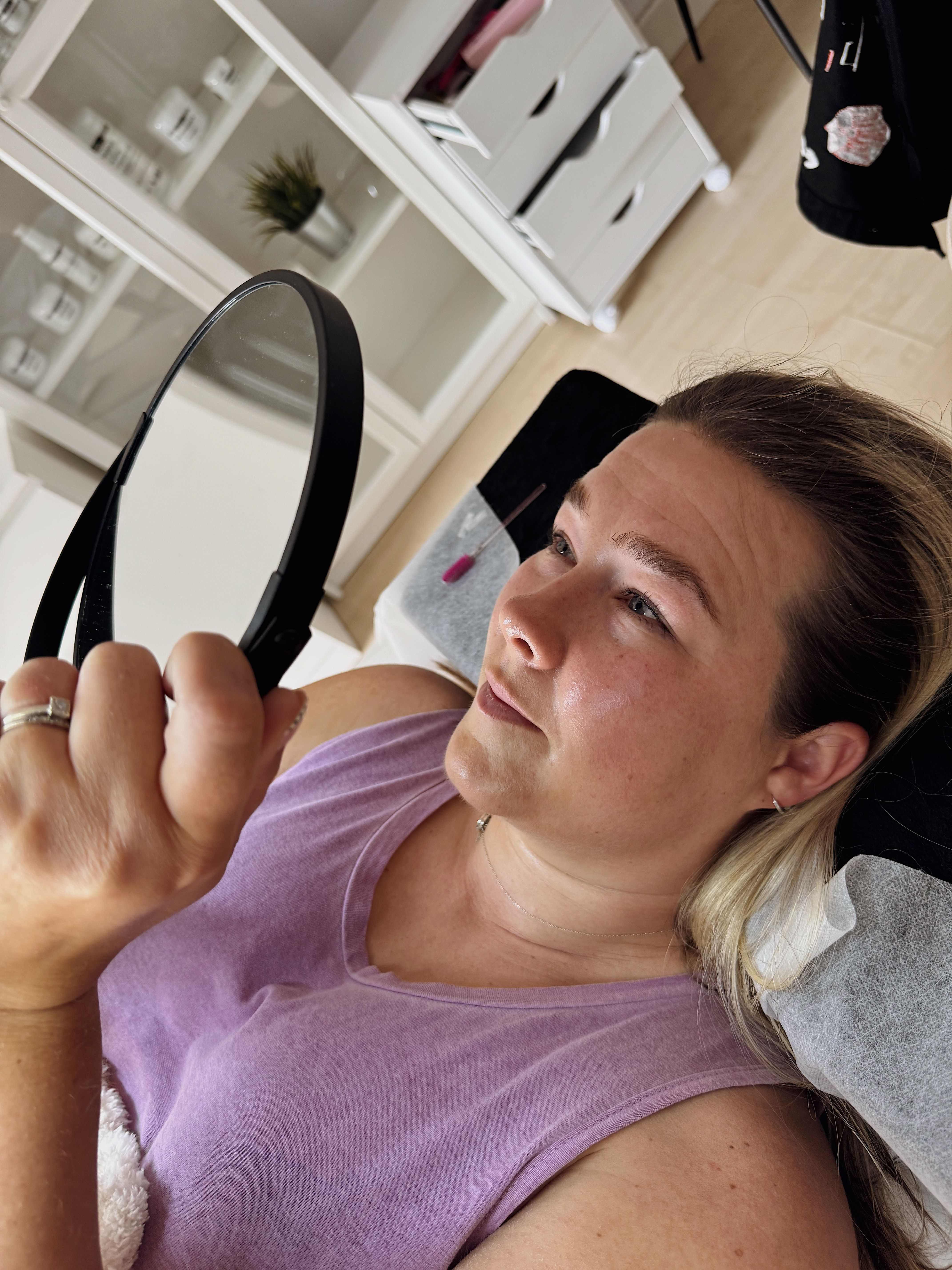 A woman holds a mirror in her hands after eyelash lamination and looks at the result