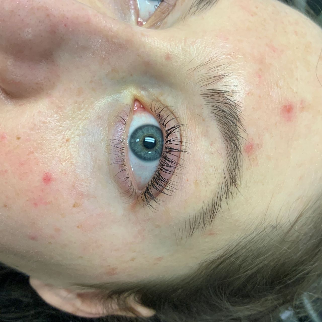 A close-up of a person's face showing blue eyes with visibly curled eyelashes.