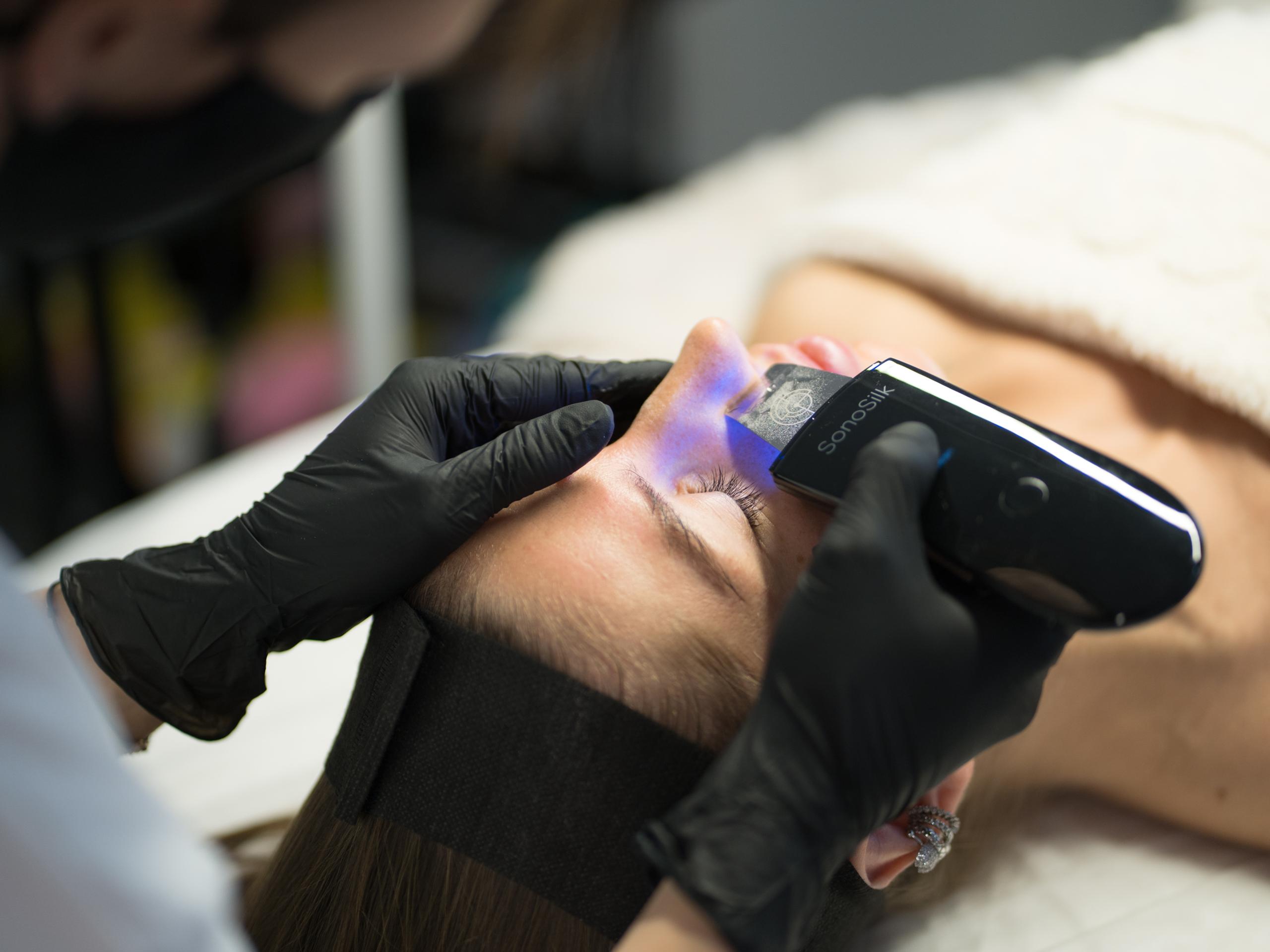 A person receives a facial treatment with a SonaSilk device emitting blue light.